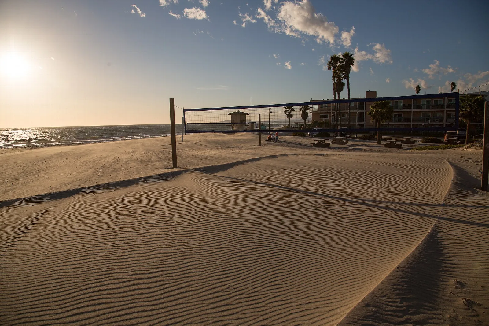 Rippled sand dune with a volleyball net and palms at low sun