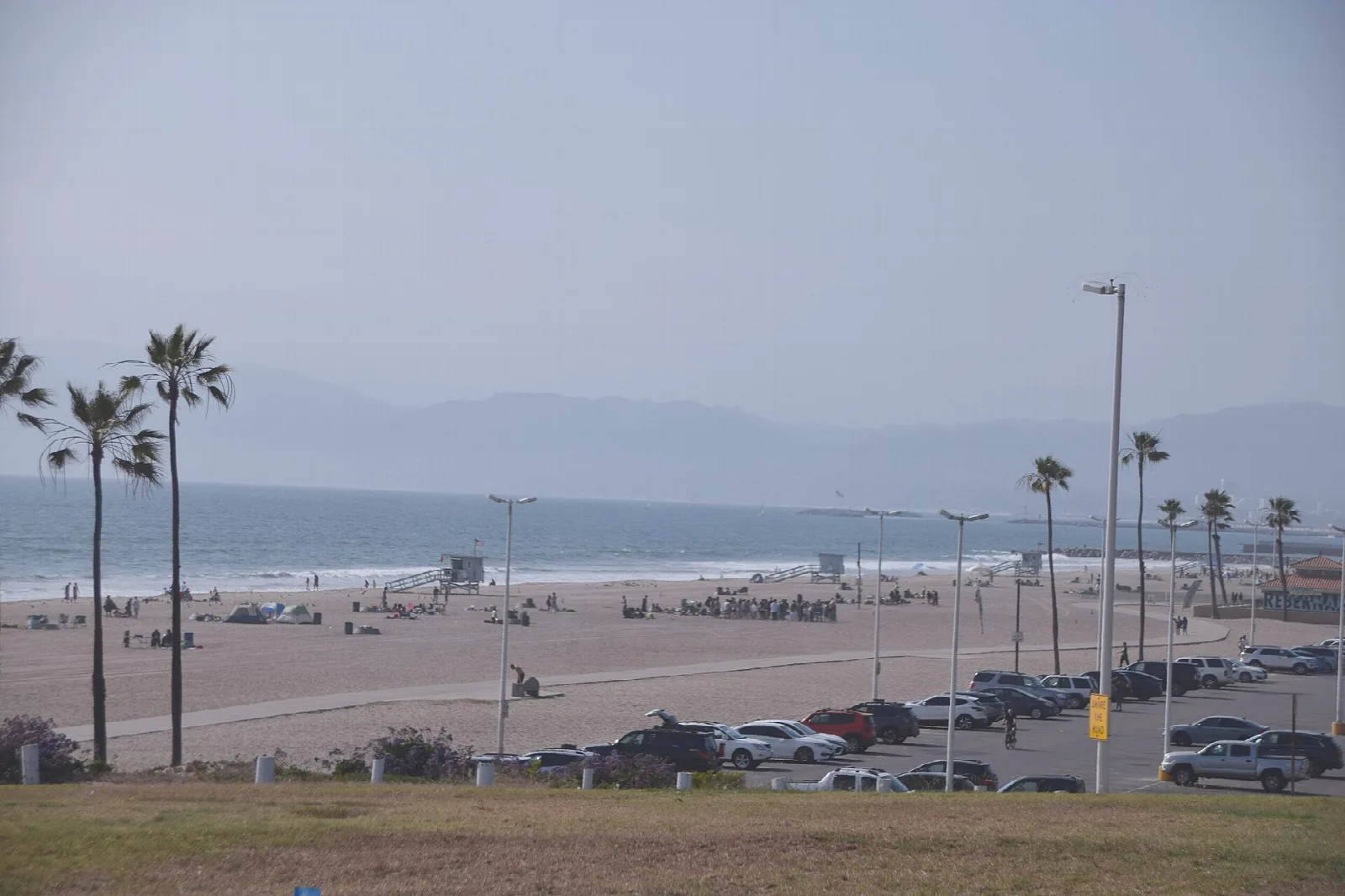 Wide sandy beach with palms, a lifeguard tower and a parking lot