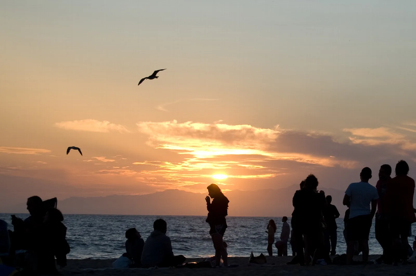 Sunset over the ocean with people silhouetted on the sand