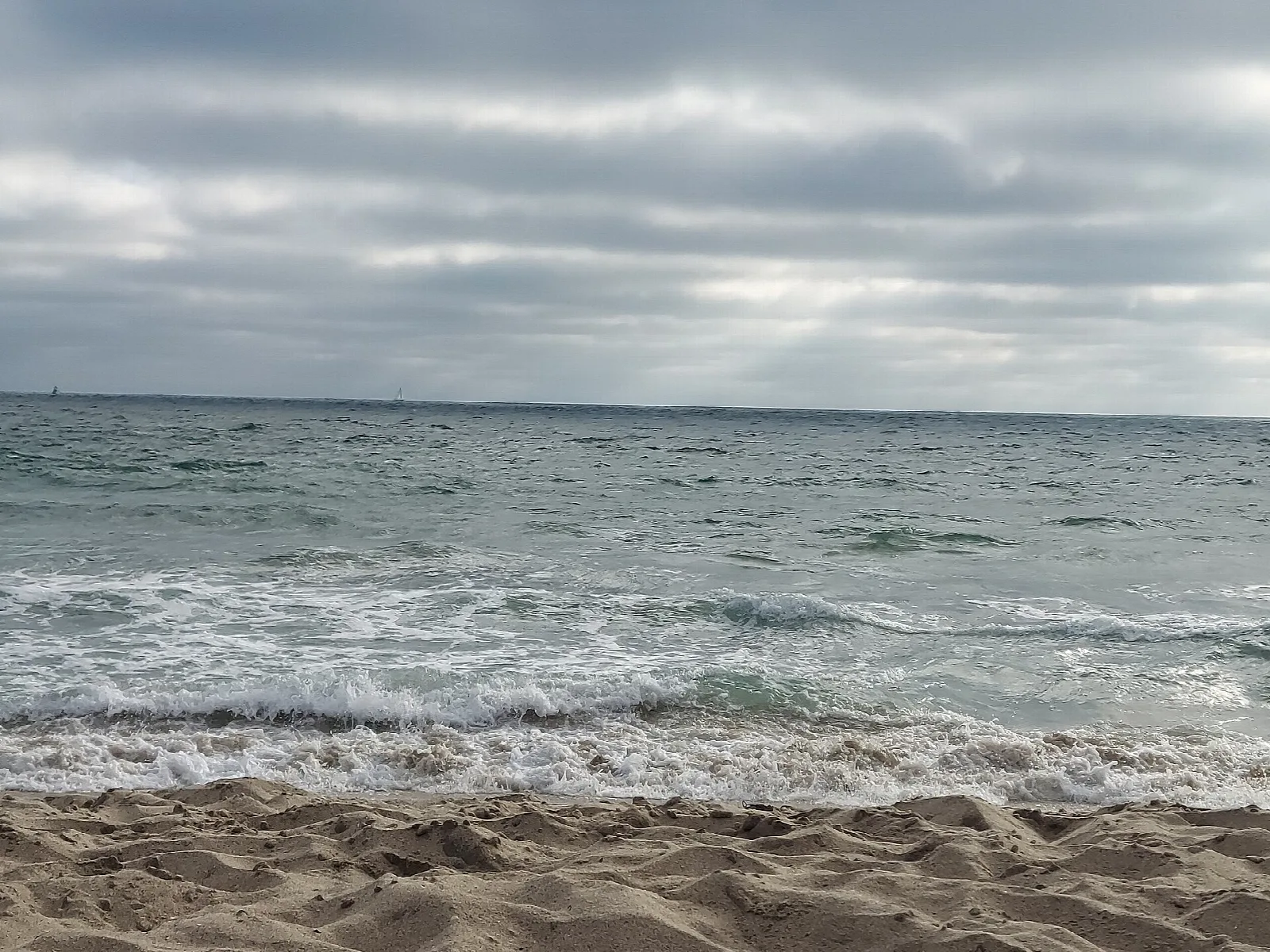 Gray surf rolling onto a sandy beach under cloud