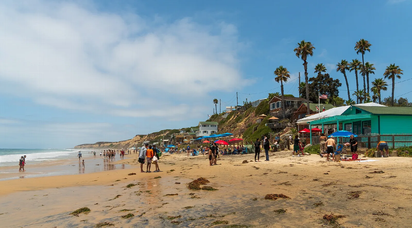 Beach with people, palm trees and a green beach building