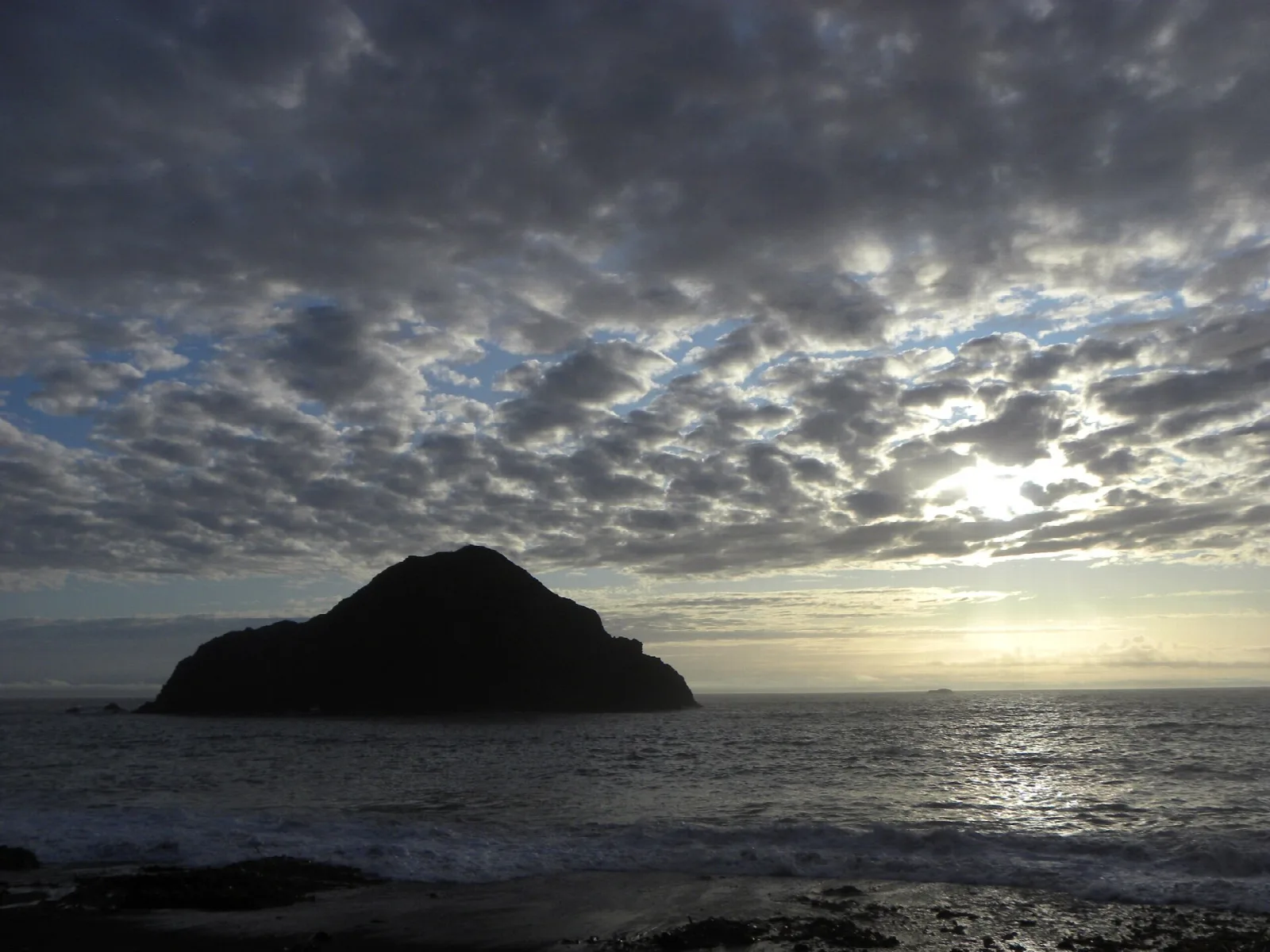 Dark island silhouette under a cloudy sky over the sea
