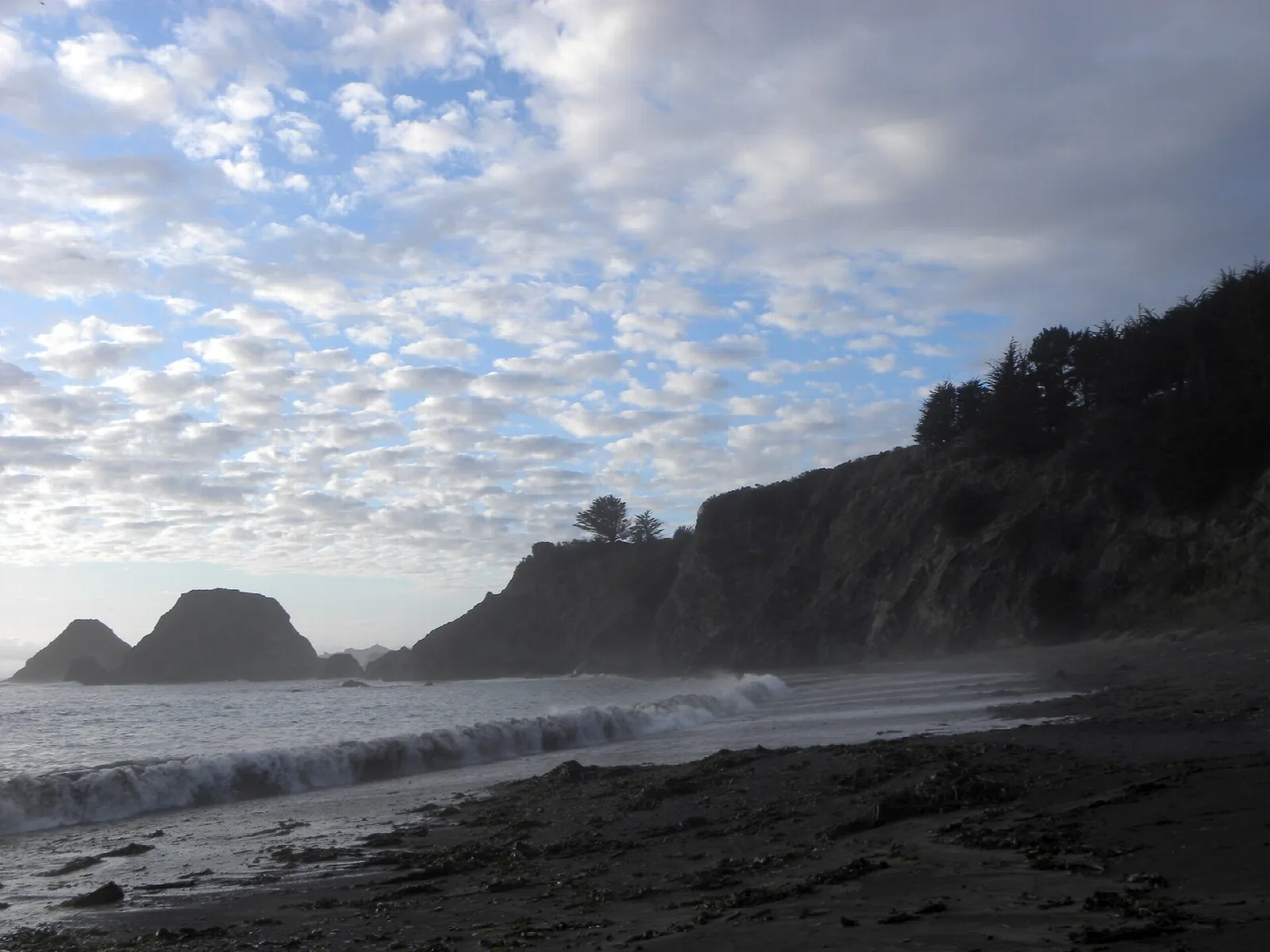 Rocky cliffs and sea stacks above a dark beach under cloud