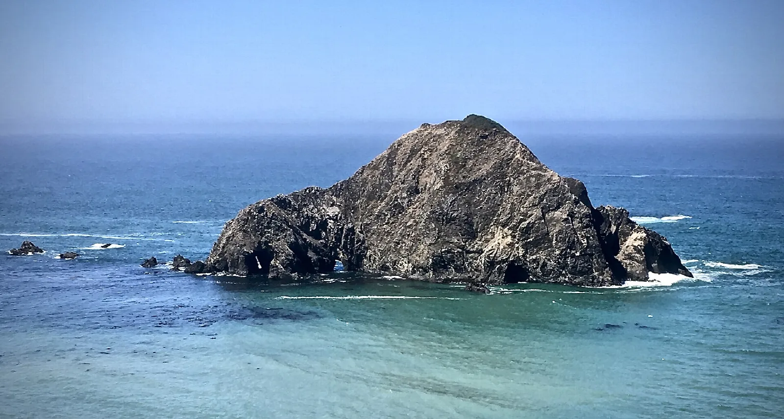 Dark sea stack rising from blue water