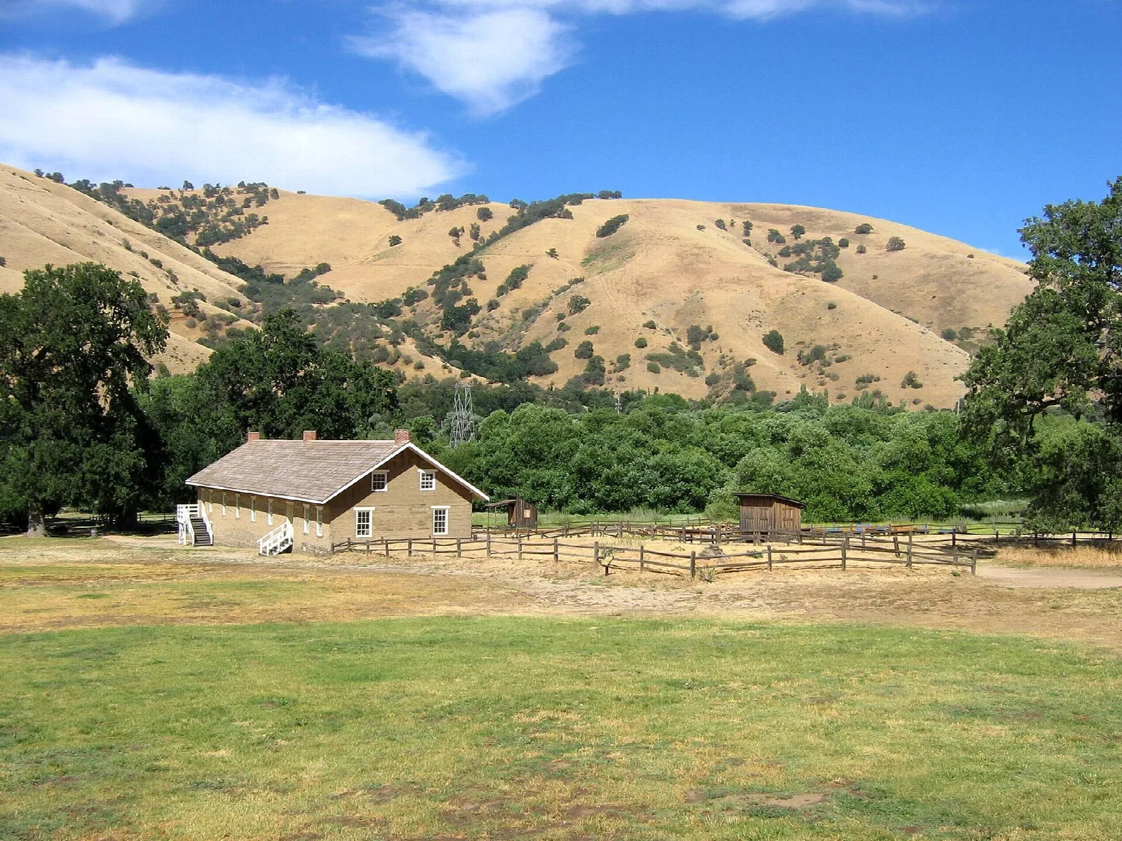Long adobe barracks on a green lawn with golden hills behind
