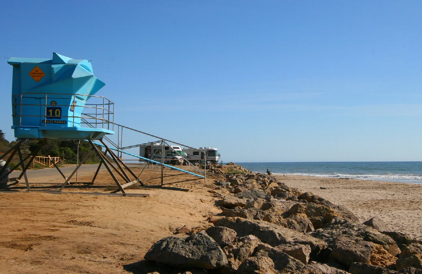 Blue lifeguard tower and campsites above a rocky, sandy beach