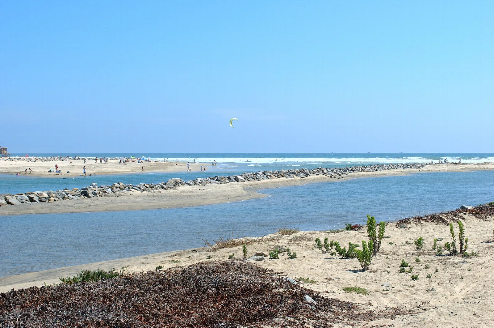 River mouth meeting the sea beside dune plants and a rock jetty