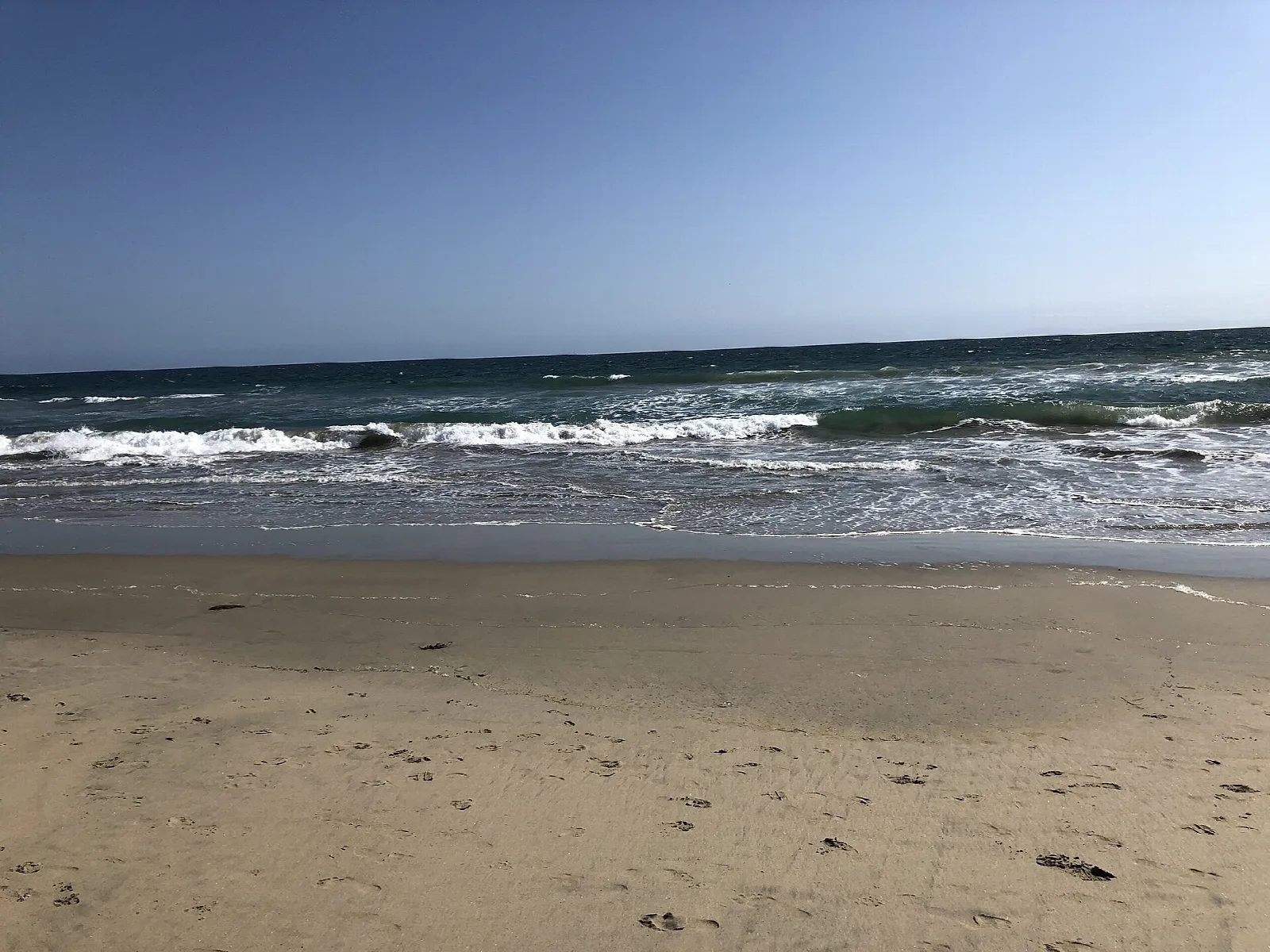 Sandy beach and breaking waves under a blue sky