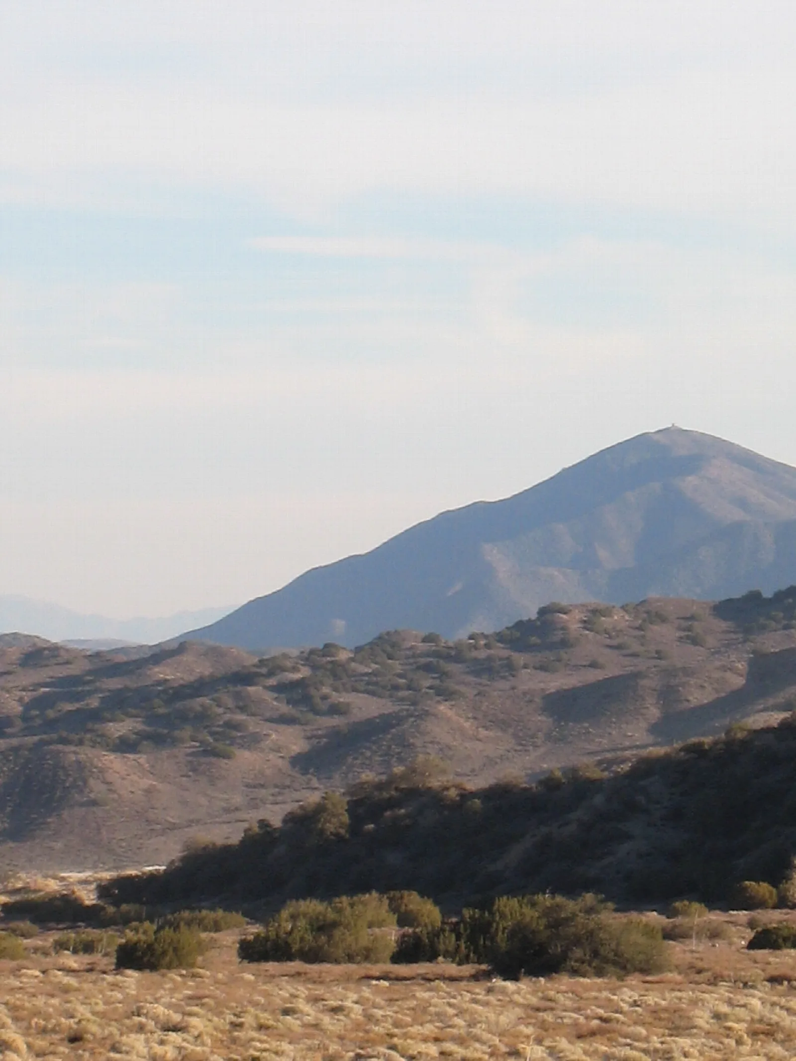 Dry brown hills with a rounded peak behind under a pale sky