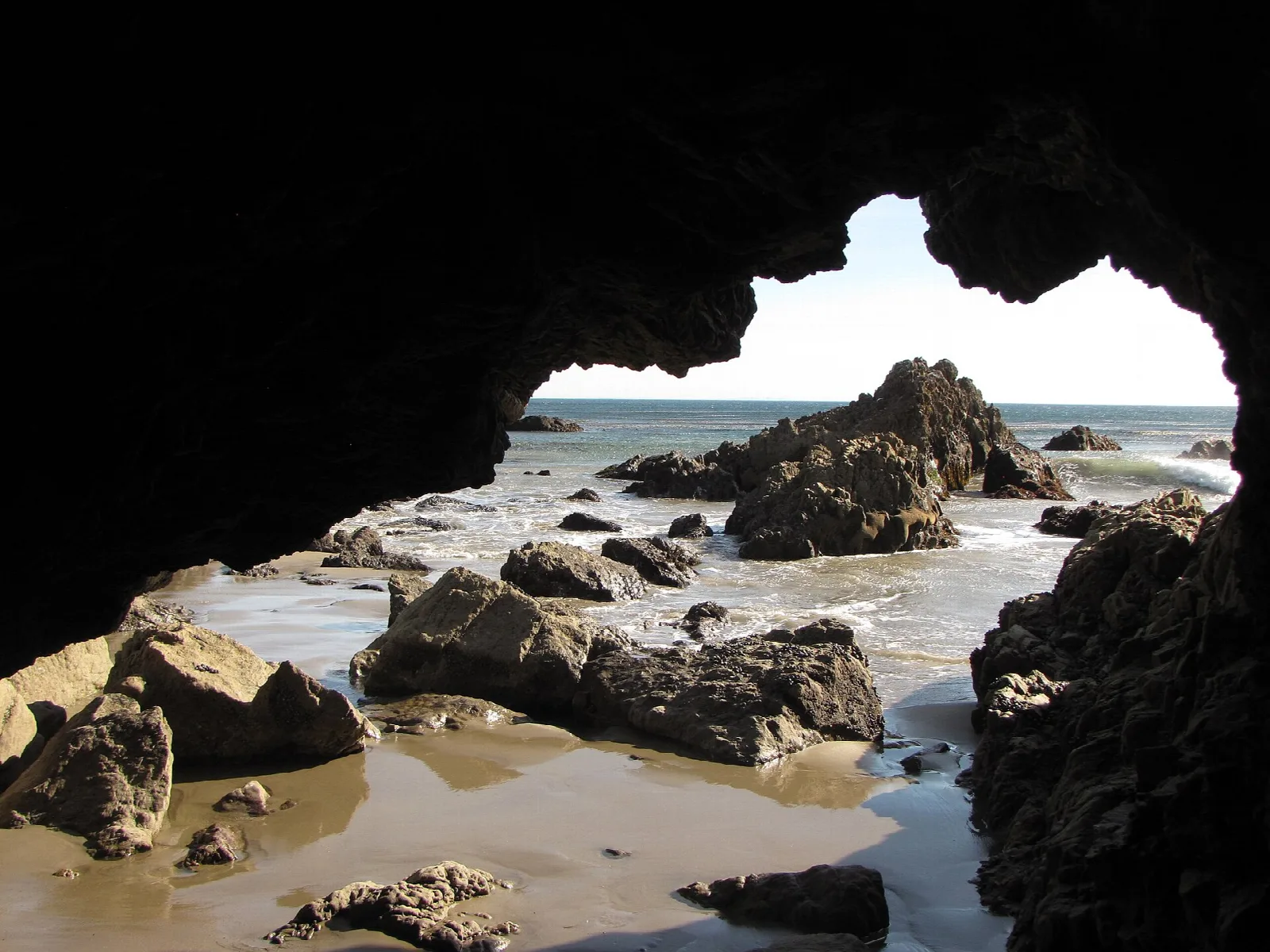 Looking out of a dark sea cave at rocks and tidal pools on the beach
