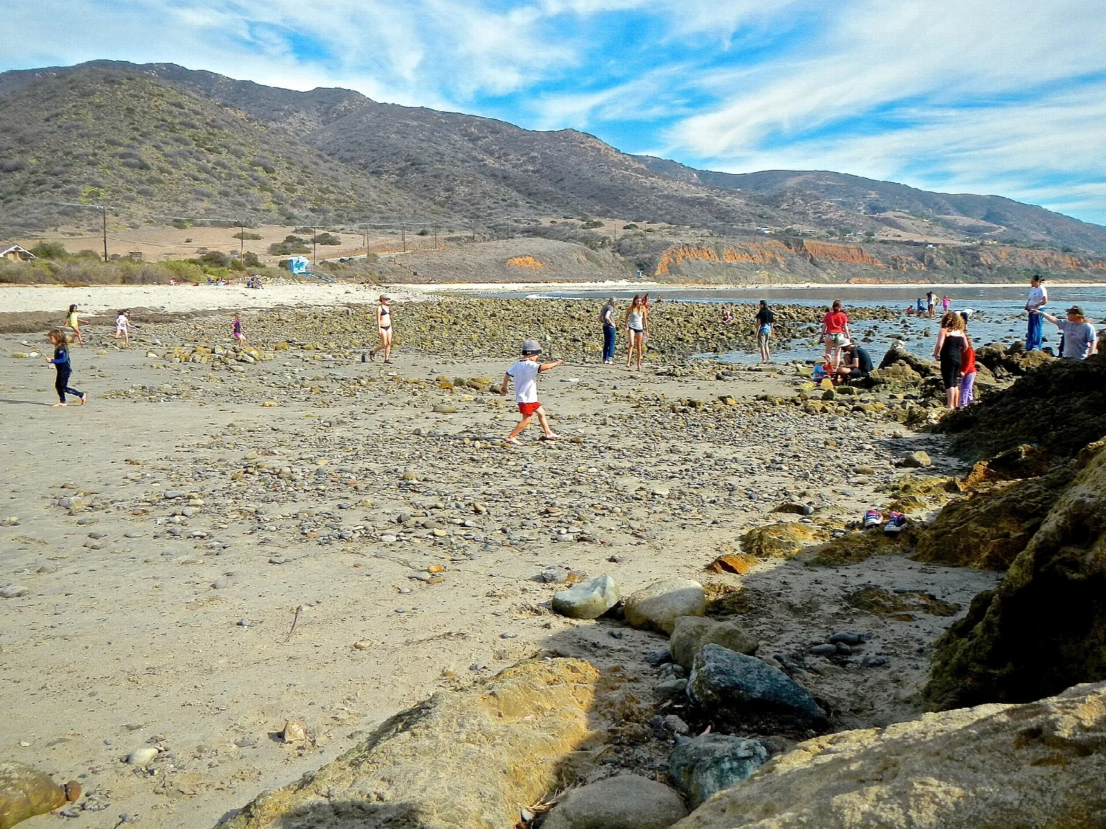 Wide beach with visitors walking along tidepools below coastal mountains
