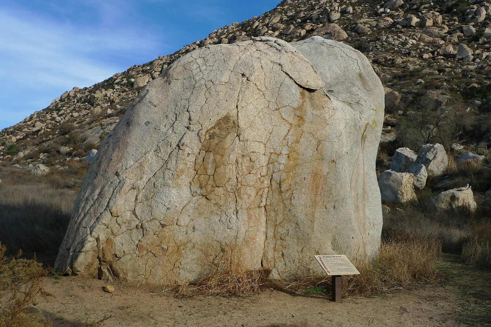 Large pale boulder on a dry hillside with a small interpretive sign