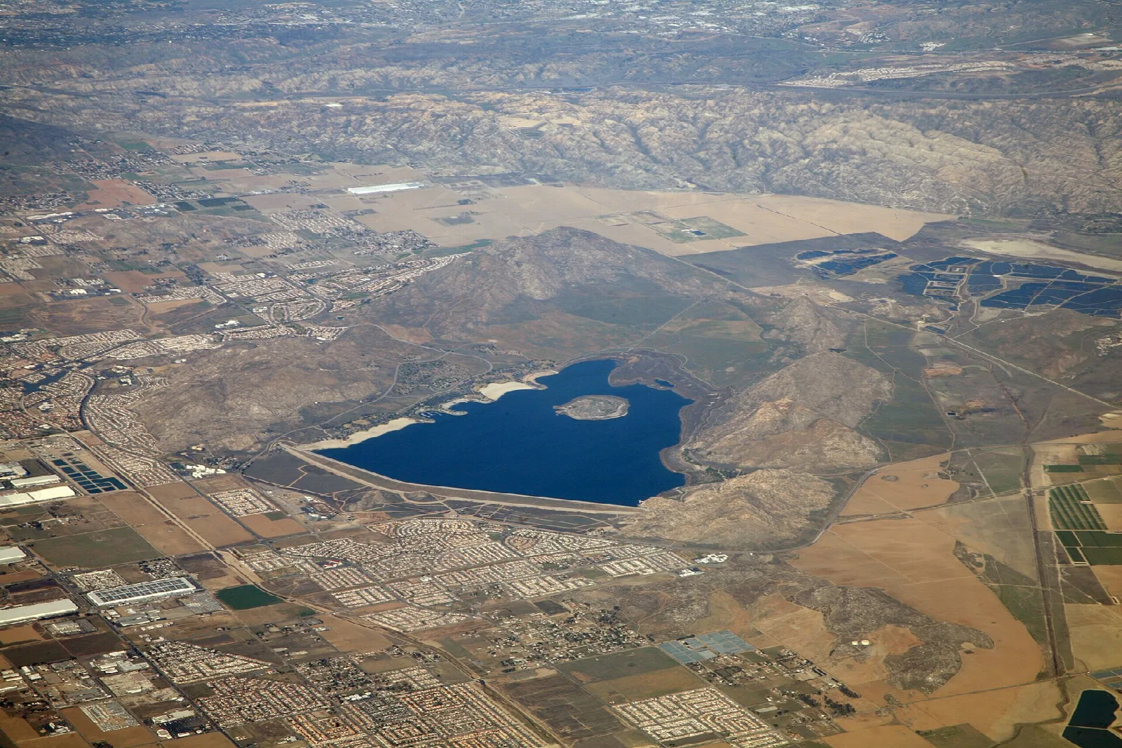 Aerial view of a blue reservoir with an island, ringed by hills and farmland
