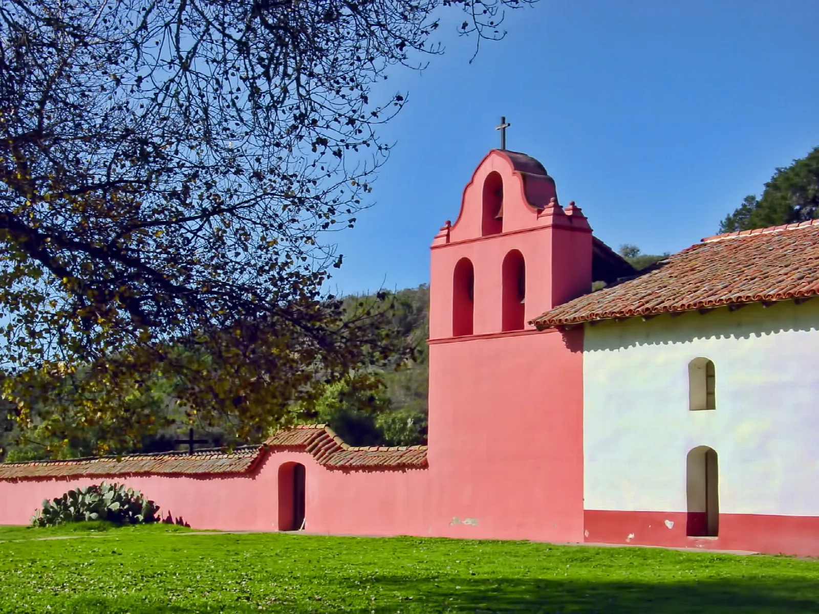 Pink mission bell tower and white wall with a tiled roof under a blue sky
