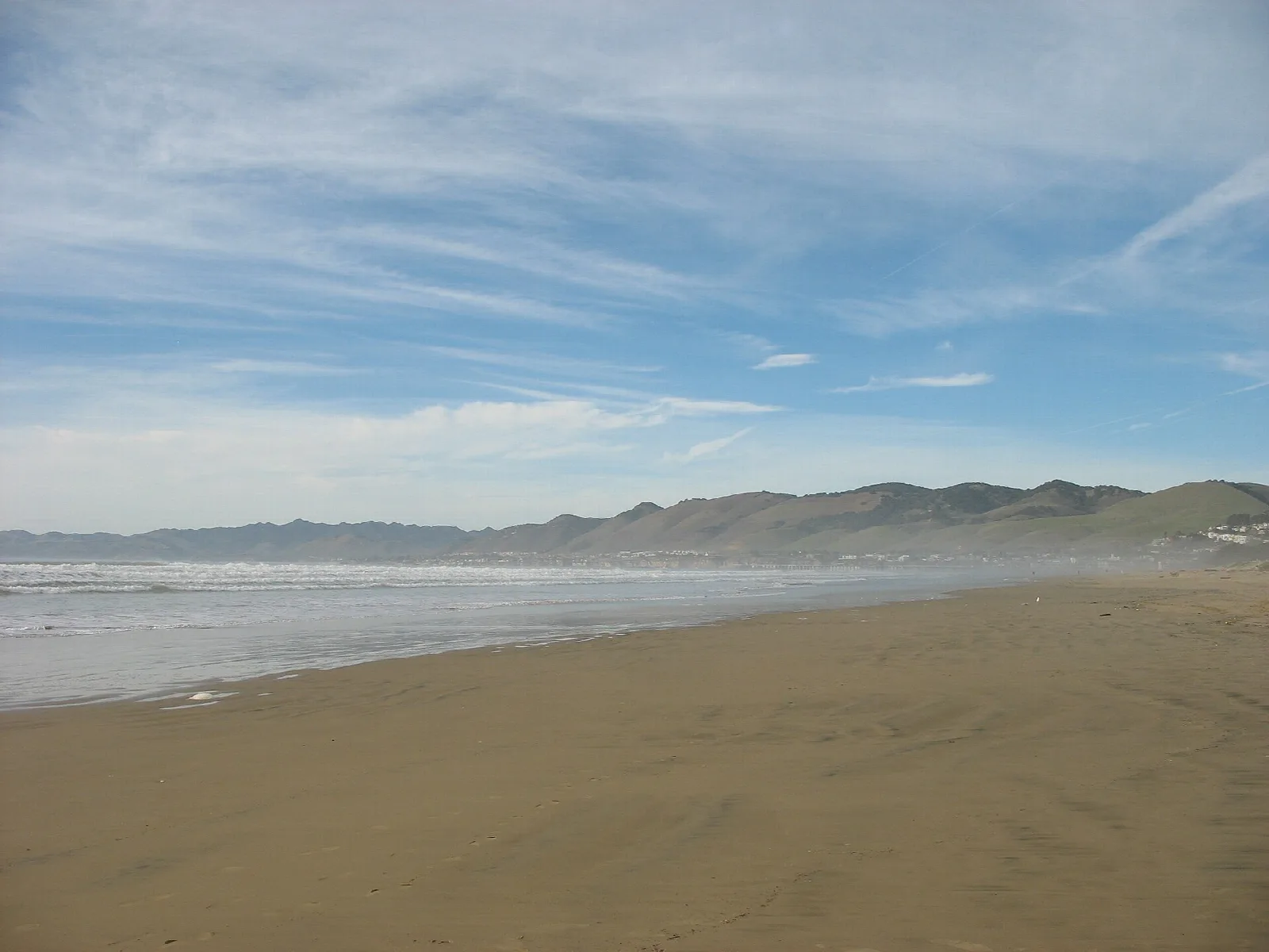 Wide sandy beach with a hazy sky and low hills in the distance