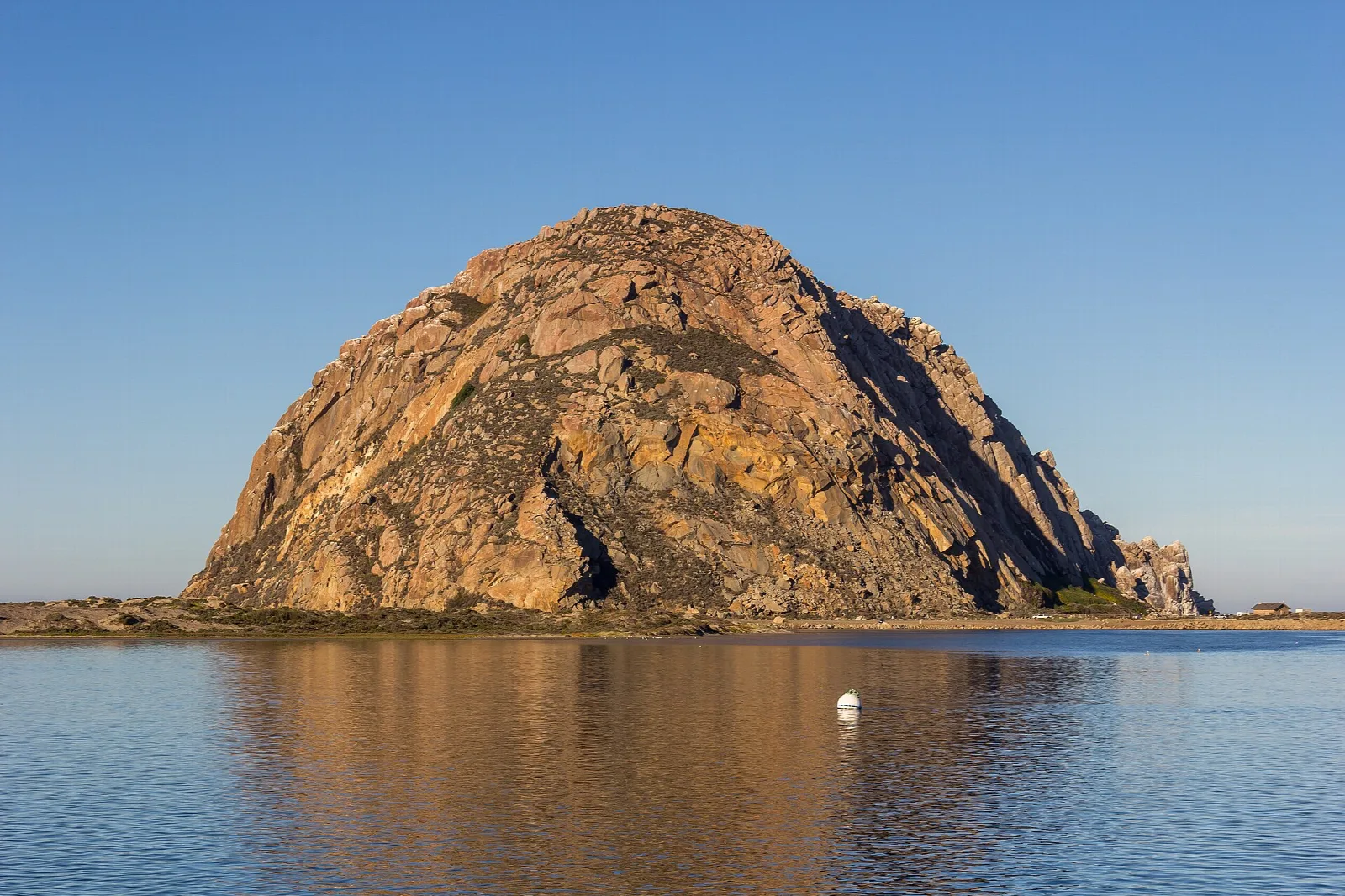 Morro Rock rising from calm water under a blue sky