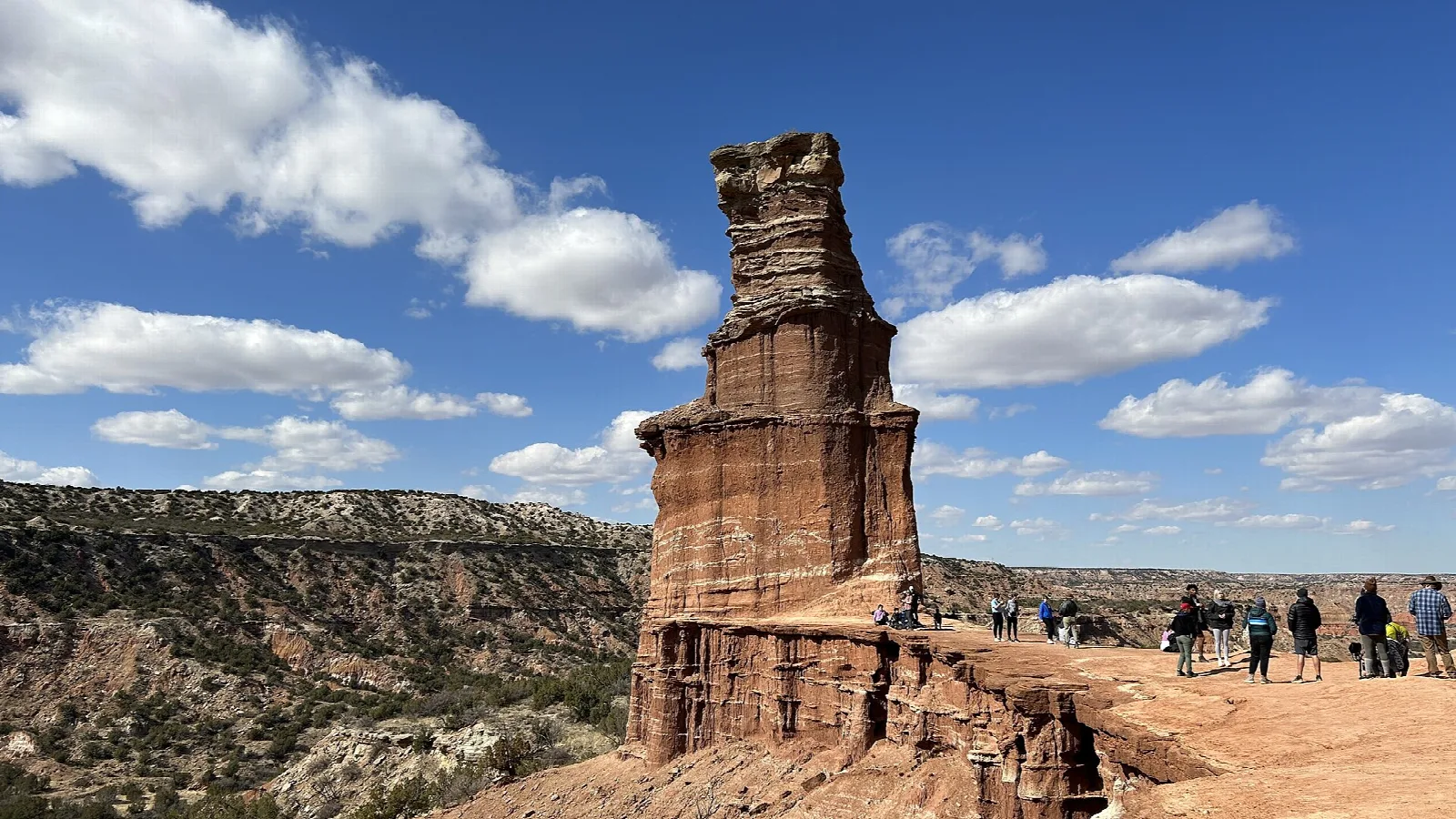 Tall red rock tower called the Lighthouse above a canyon, with visitors at its base