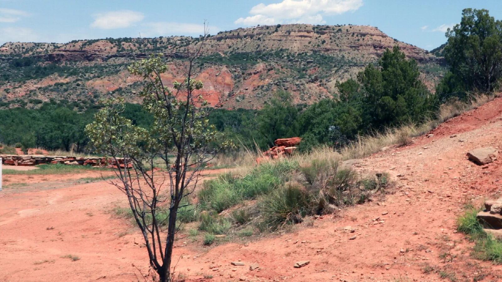 Red-banded canyon mesa above green trees and a red dirt path