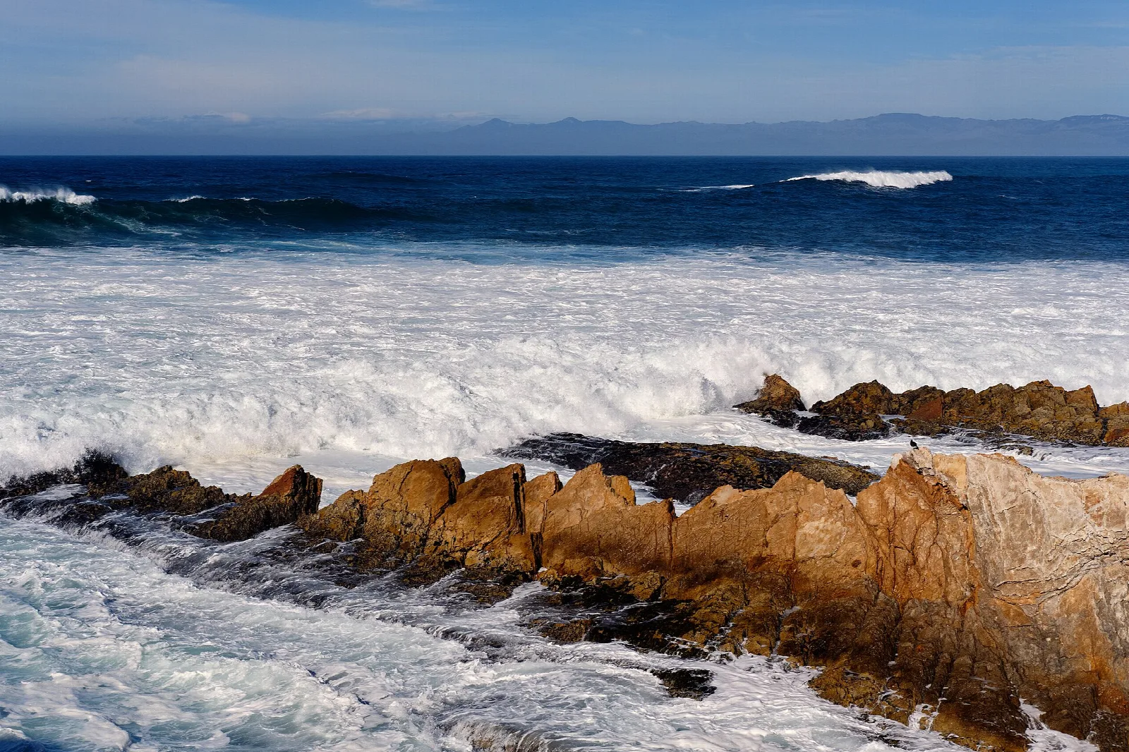 Waves breaking over orange rocks at the shoreline