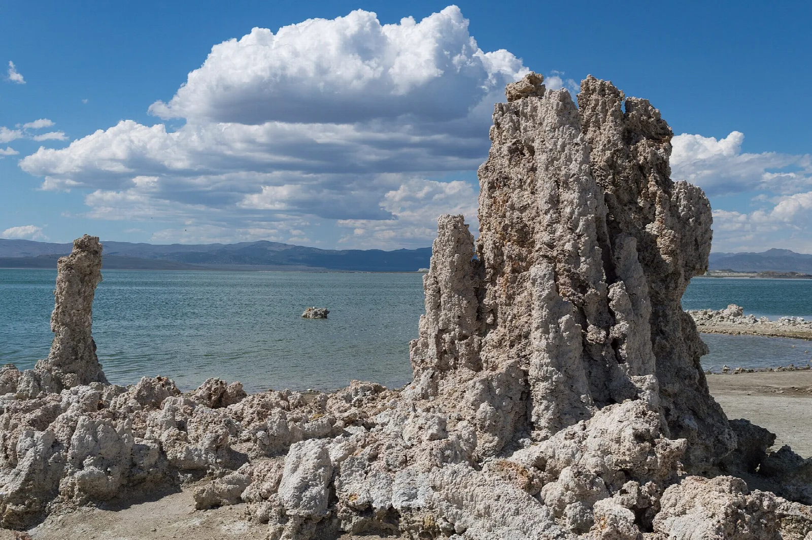 Tall tufa tower beside the lake under big clouds