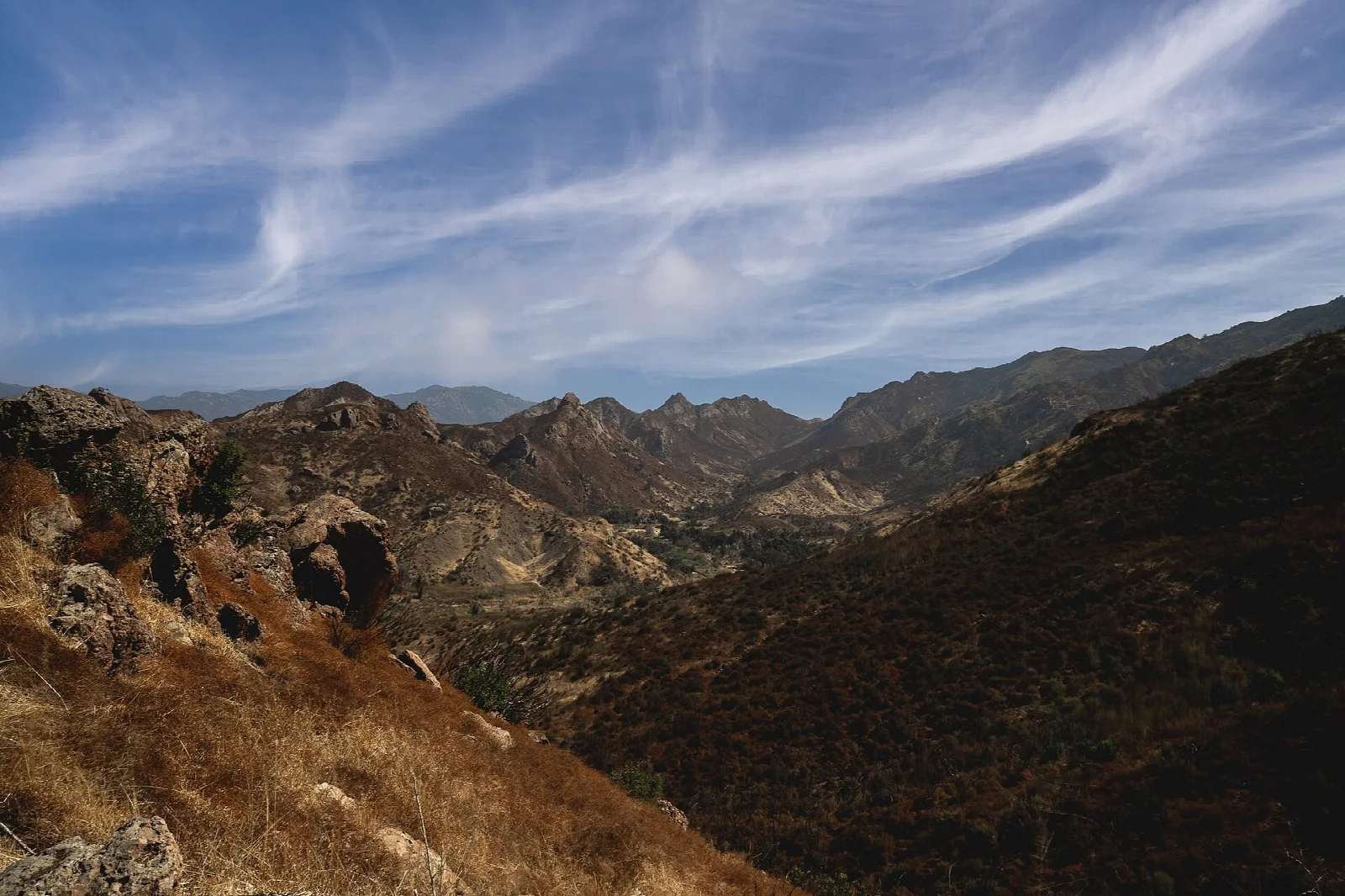 Rugged brown hills and canyons under a streaked sky