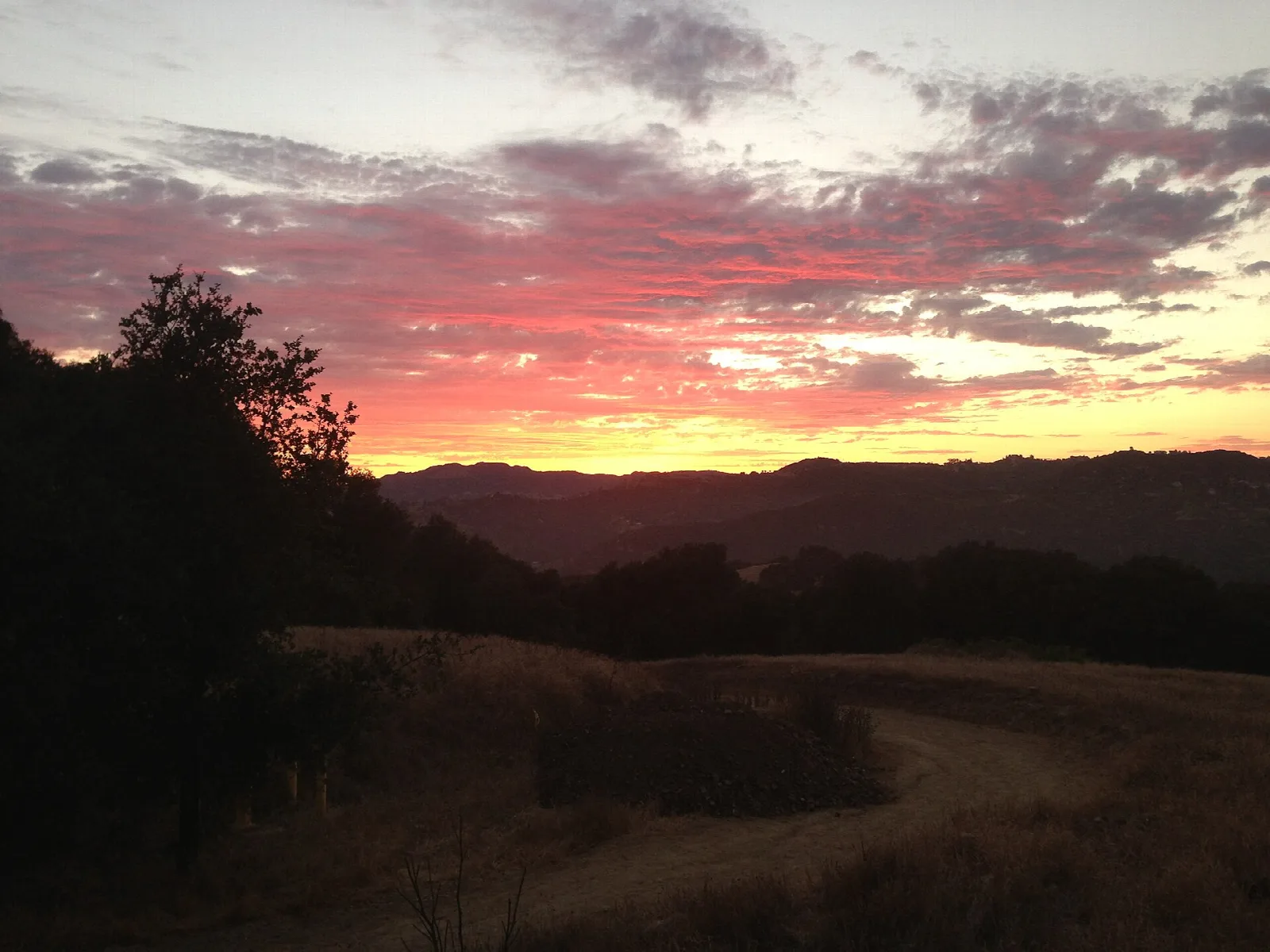 Pink sunset sky over dark hills with a dirt track in the foreground