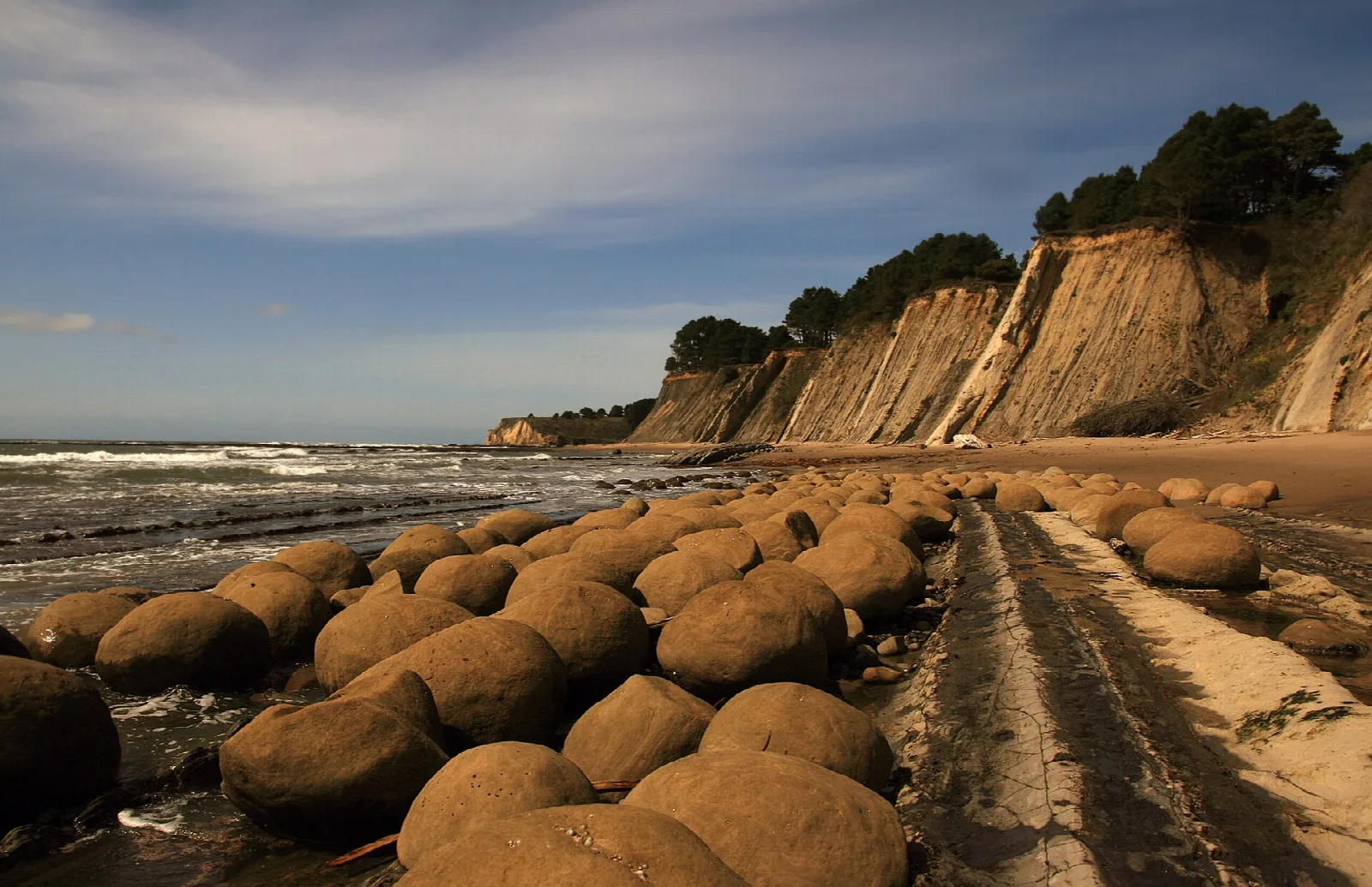 Rows of round boulders on a wet beach below tall cliffs