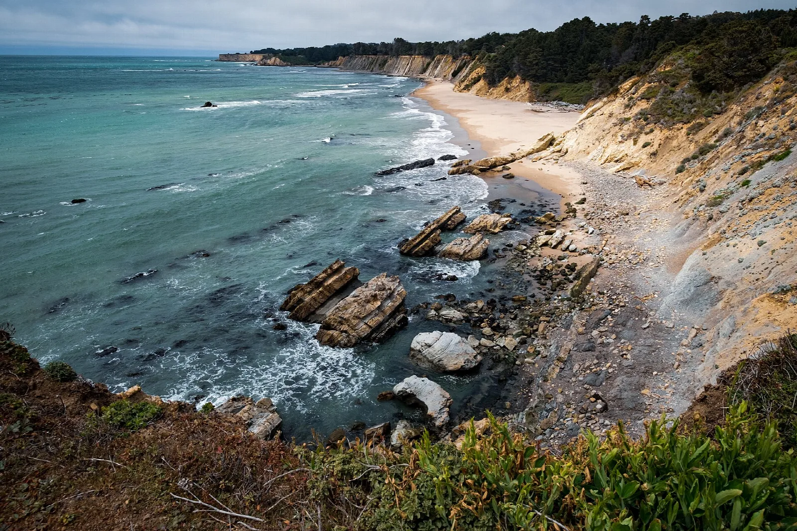 Turquoise cove with rocks, a sandy beach and cliffs seen from the bluff