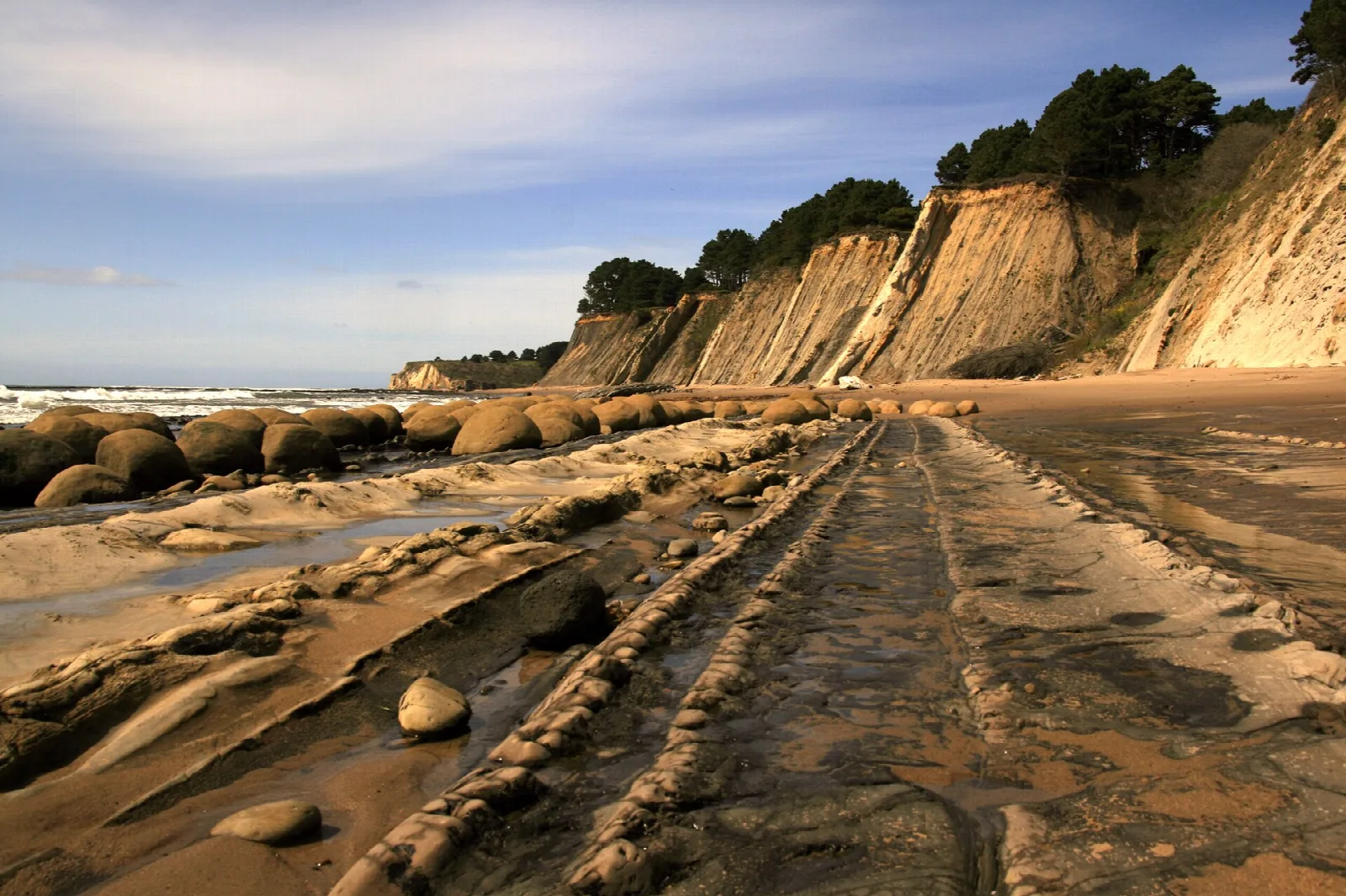 Boulder-strewn tidal flats under layered cliffs