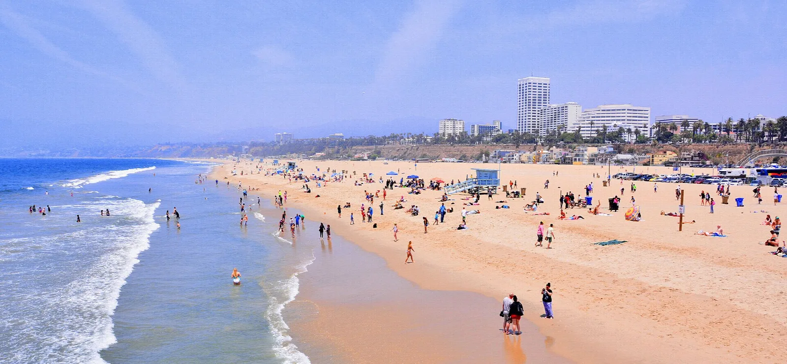Swimmers and sunbathers on a wide beach beside the surf