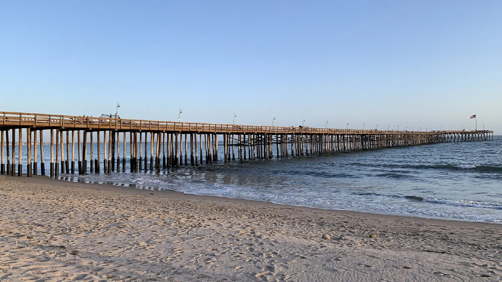 Long wooden pier stretching over the water from a sandy beach at sunset