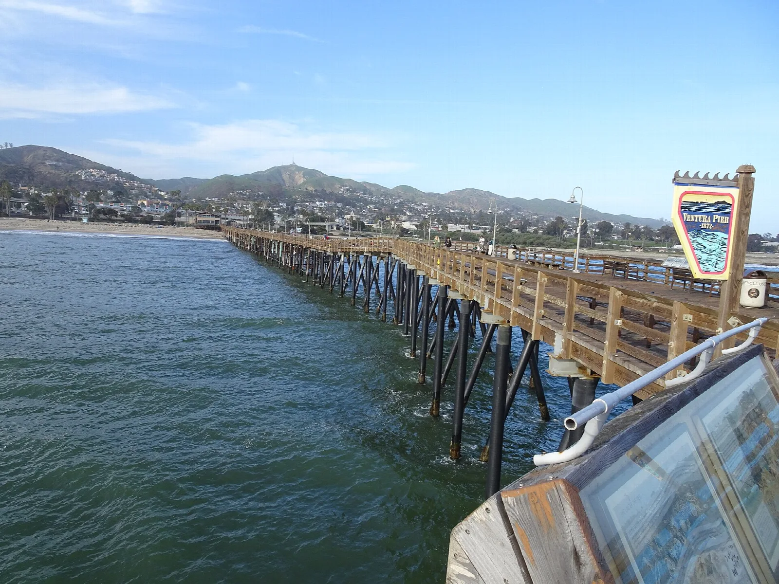 Wooden pier over green water with town and hills in the distance
