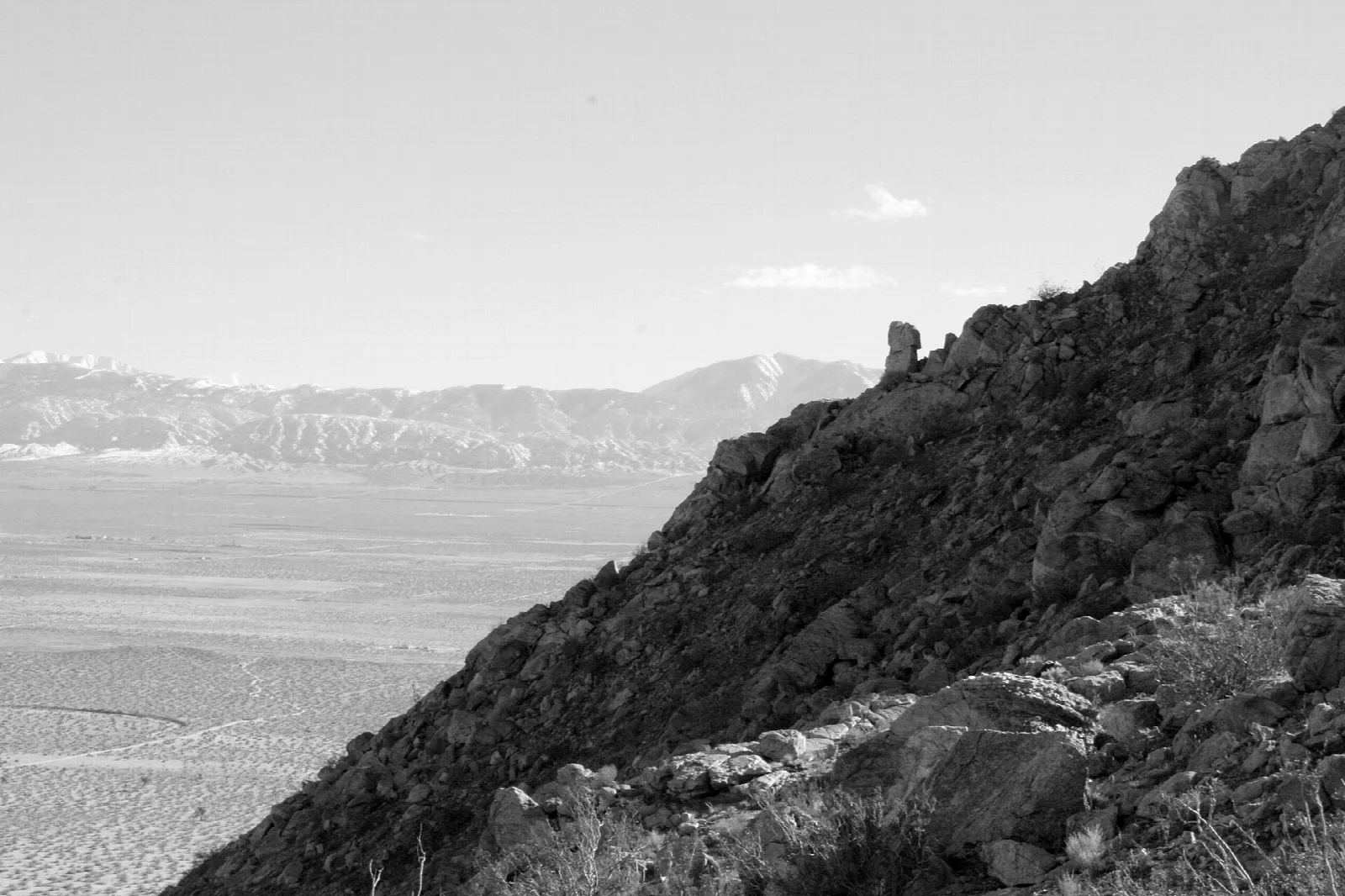 Black and white view of a rocky slope over a desert valley