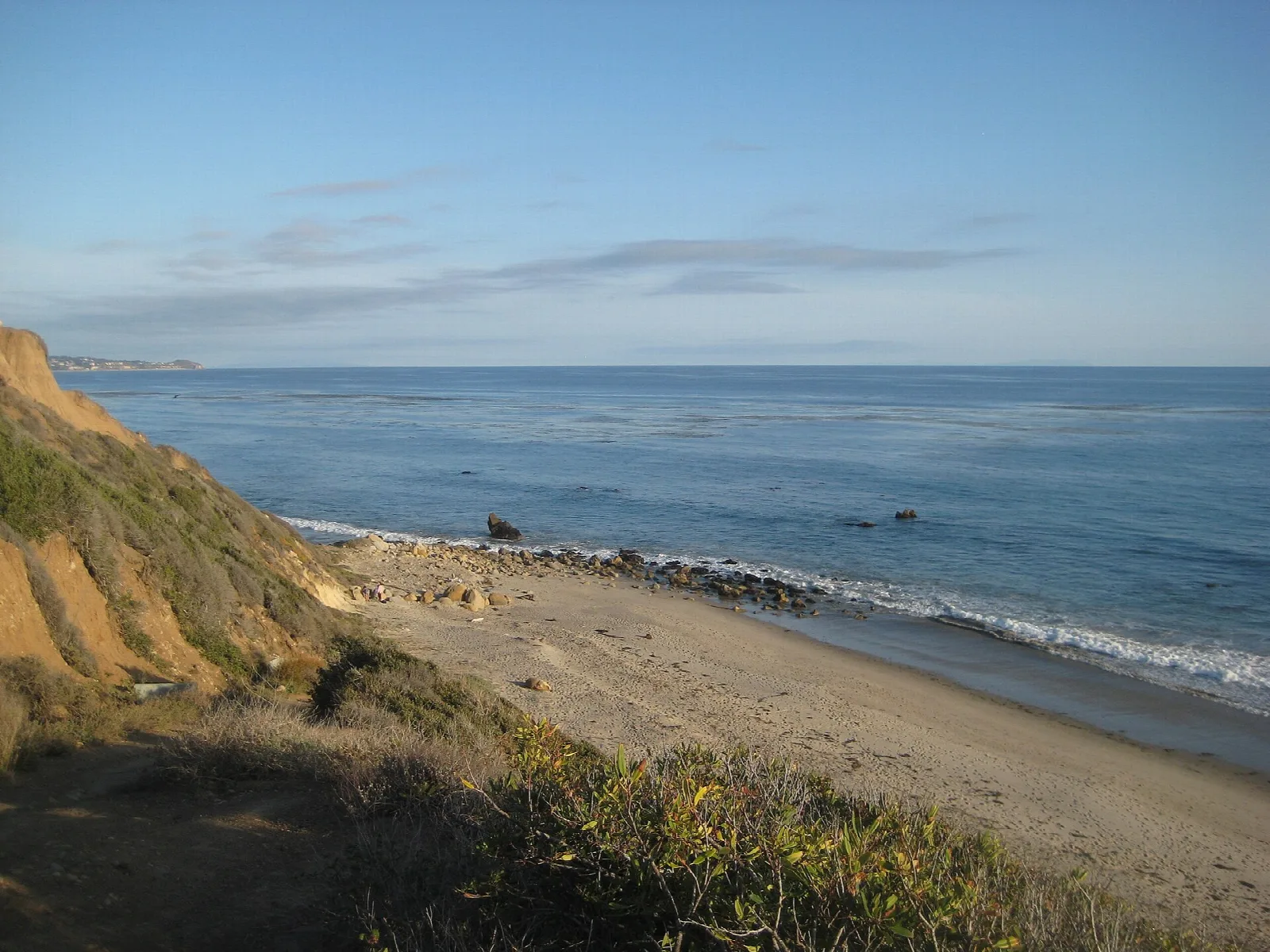 Sandy beach with surf and a grassy bluff on the left