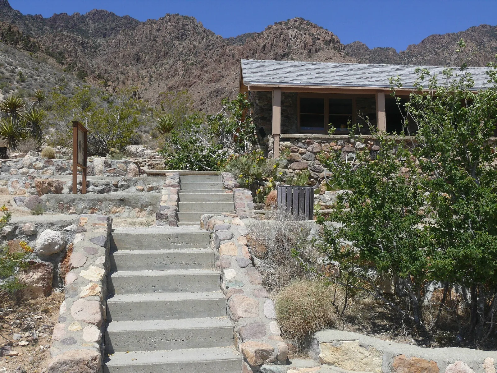 Stone visitor center building up a stone stairway with rocky mountains behind
