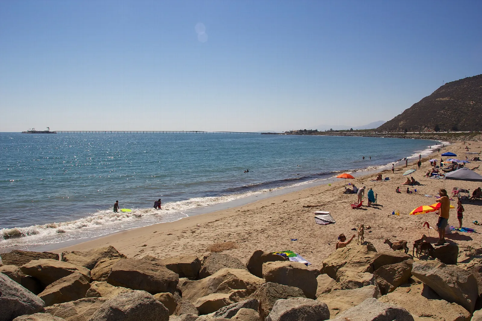 Crowded sandy beach with rocks and a distant pier