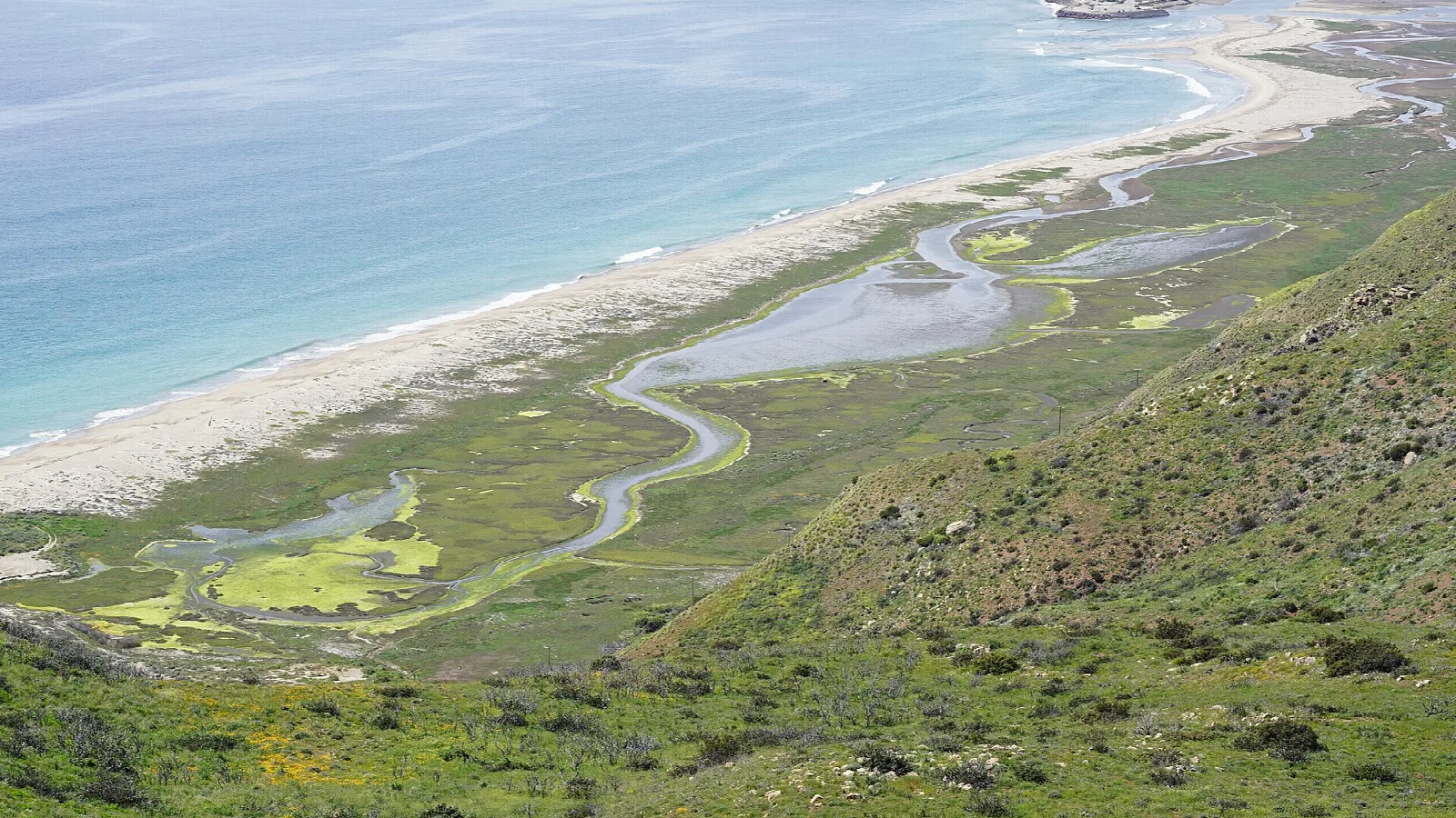Winding lagoon channel and long beach seen from a hillside
