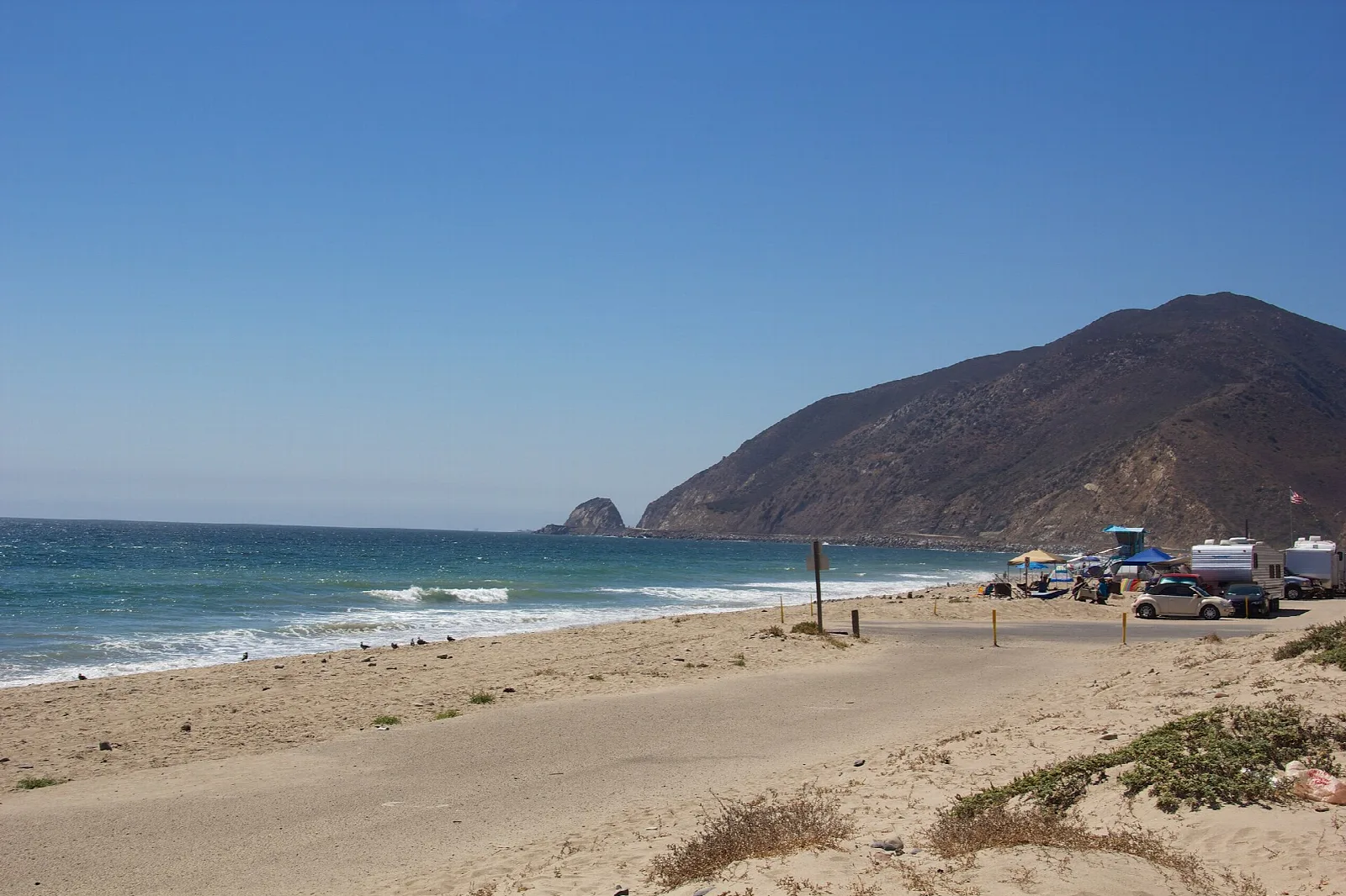 Sandy beach with cars parked and a mountain meeting the sea