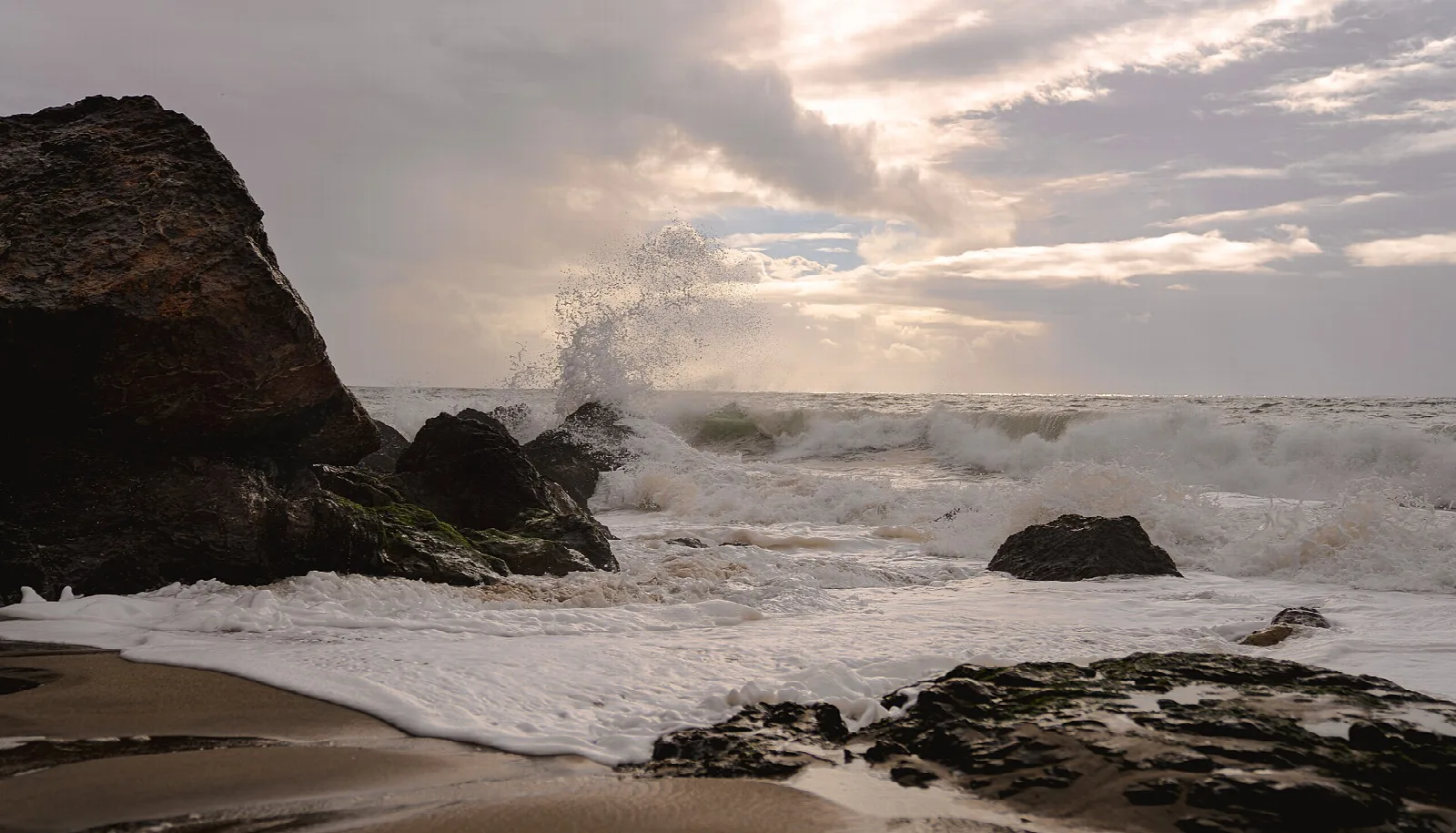 Waves breaking around dark rocks on a sandy beach