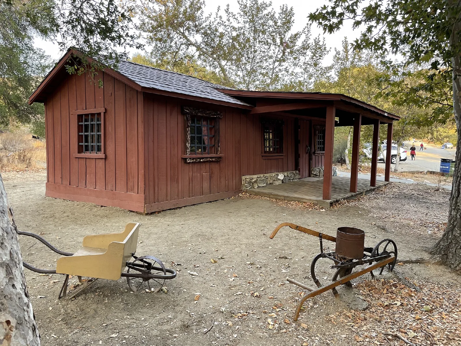 Red wooden cabin with a porch and old farm tools in a dry yard