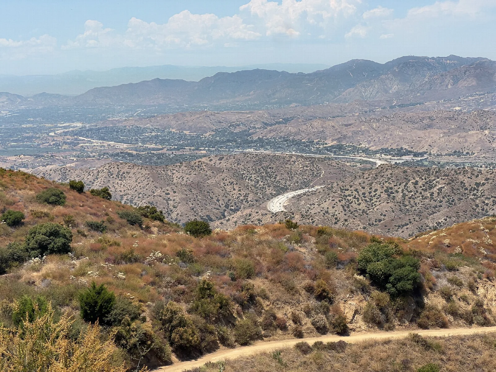 Dry brushy hillside with a dirt trail above a wide valley and distant mountains