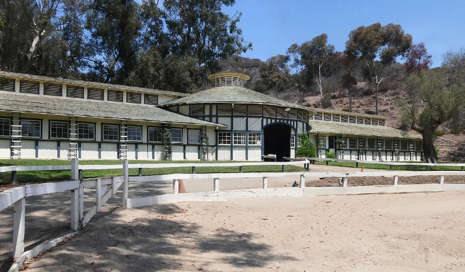 Long white horse stable beside a riding ring