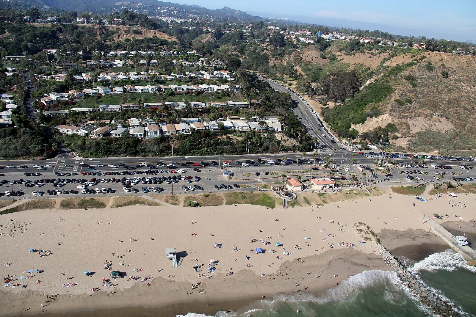 Aerial view of a sandy beach with a parking lot and hillside homes above