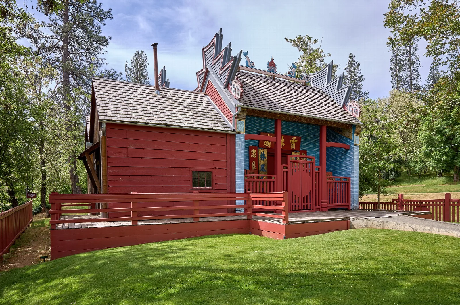 Red and blue Chinese temple with a gabled roof among trees and lawn