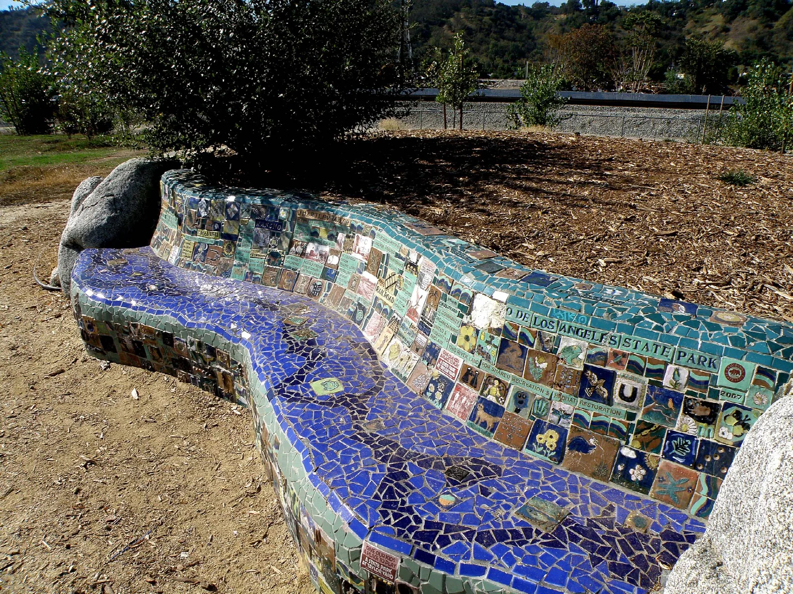 Curving mosaic tile bench under a tree