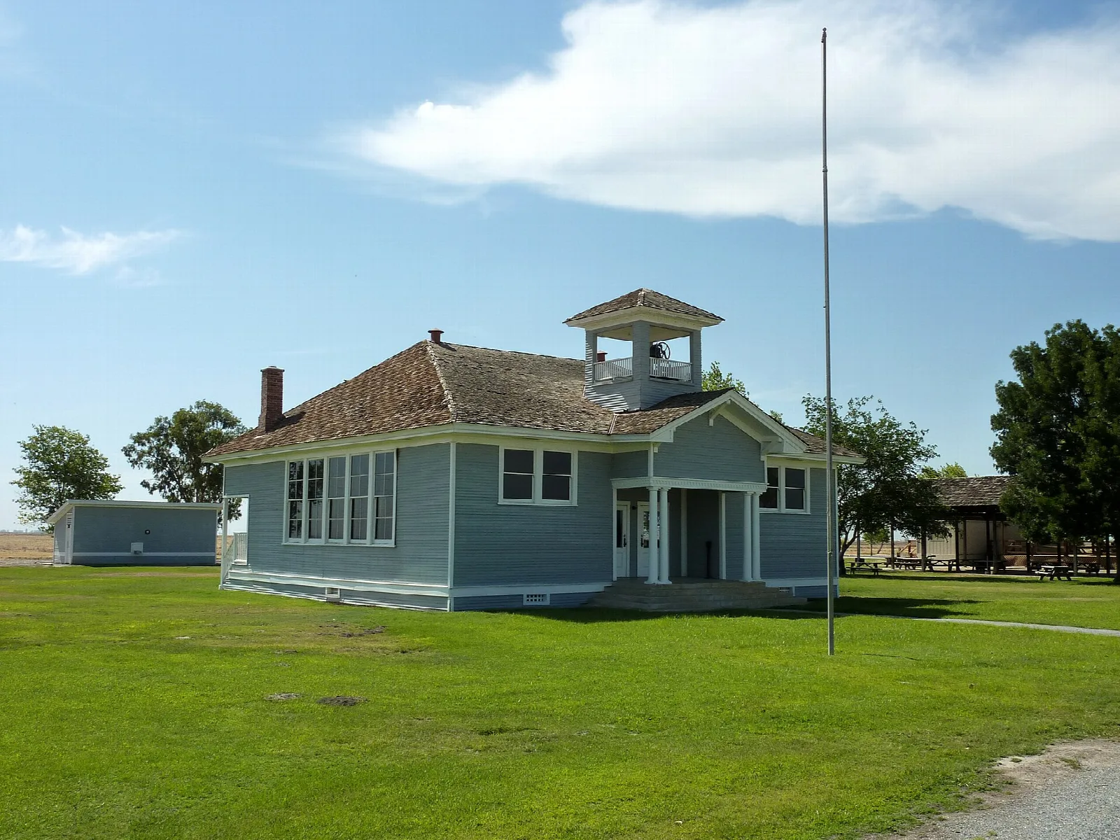 Blue-green schoolhouse with a bell tower on a green lawn