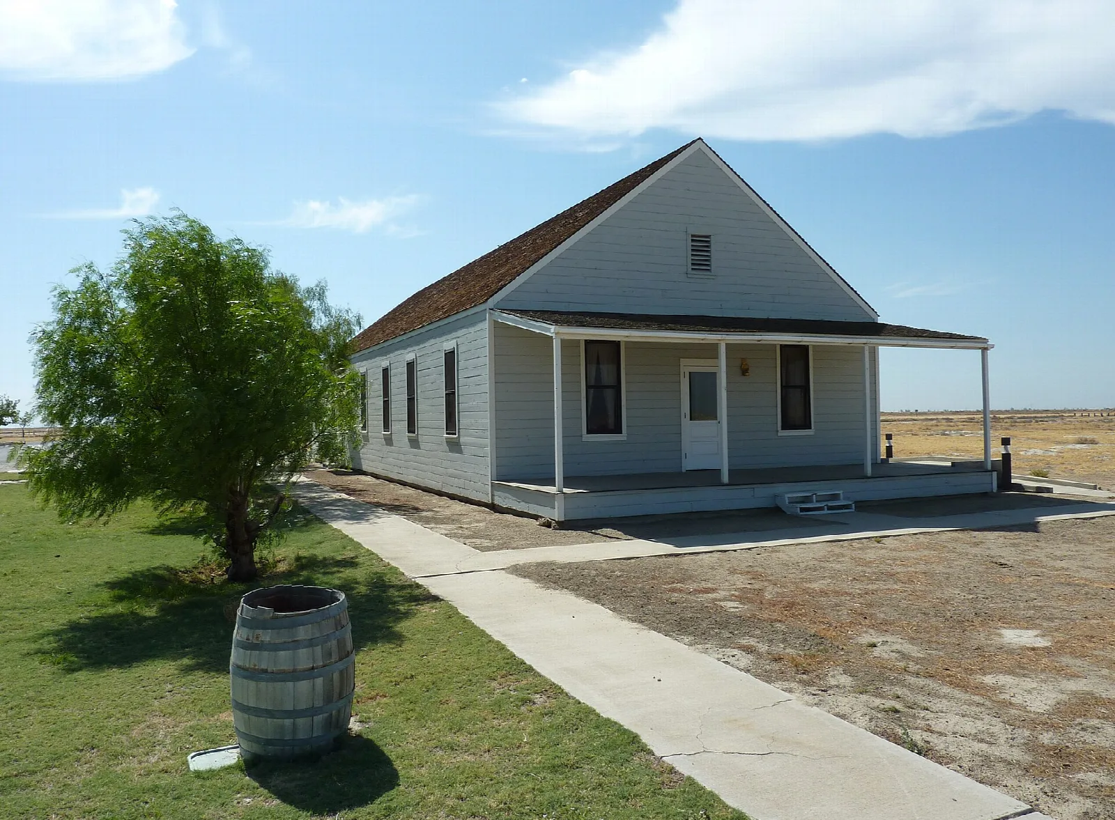 Gray wooden hotel with a porch and a tree beside it