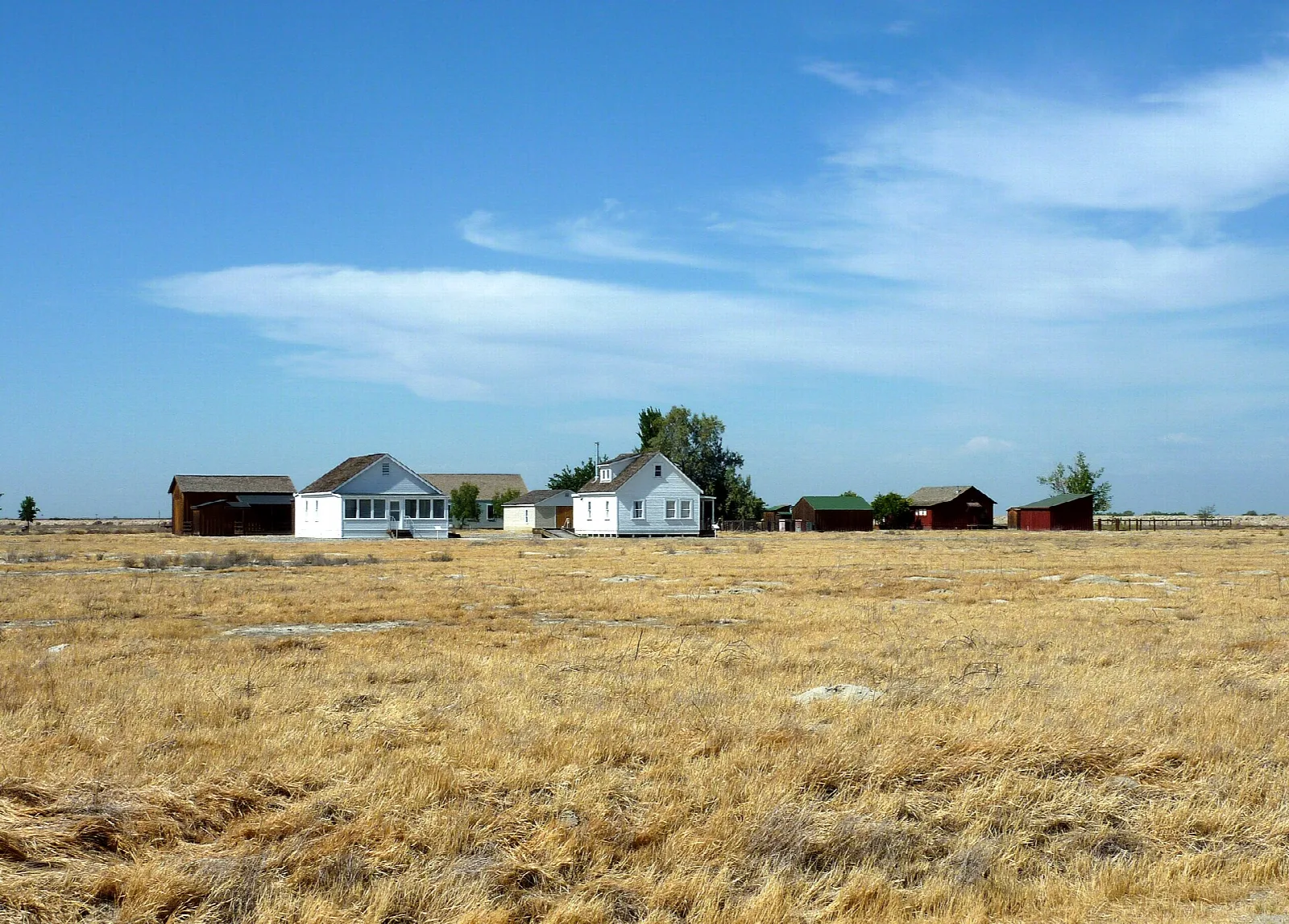 Small white buildings across a dry golden field under a big sky