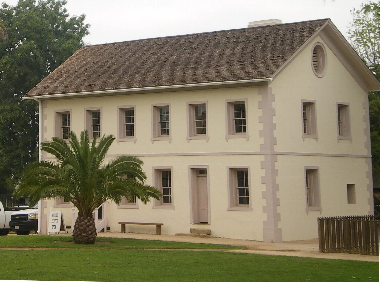 Two-story pale limestone building with a palm tree beside it