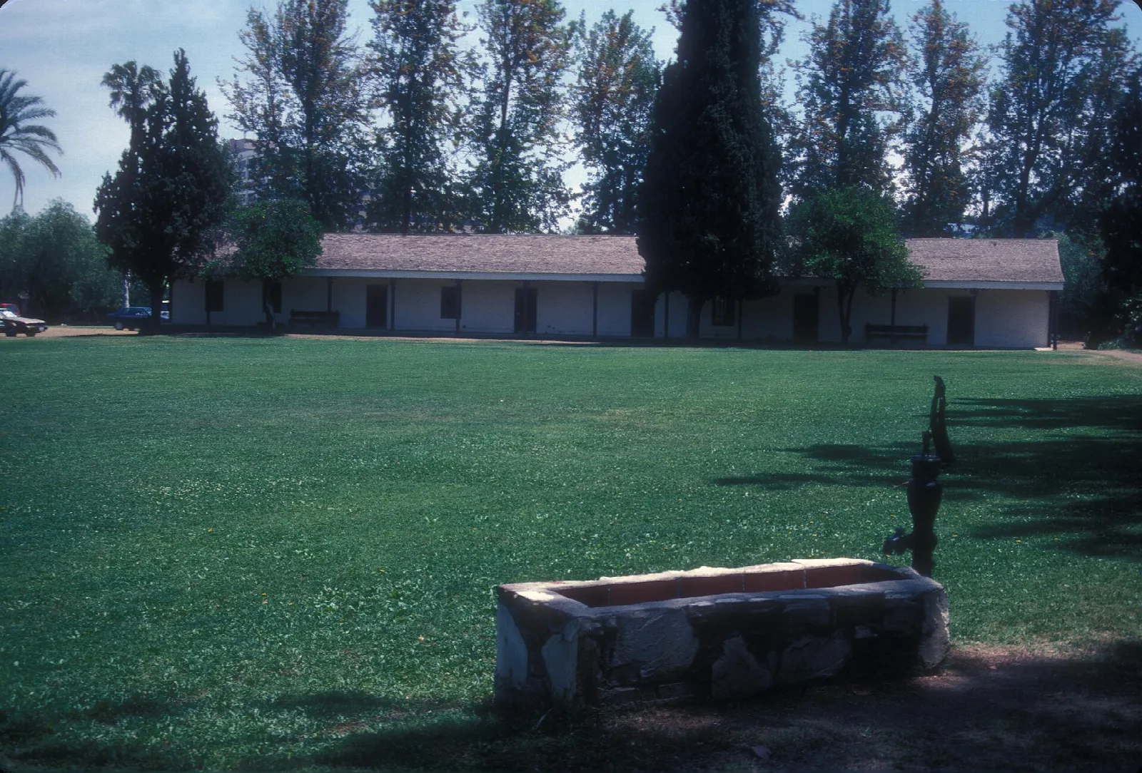 Green lawn and a low adobe building behind a stone trough